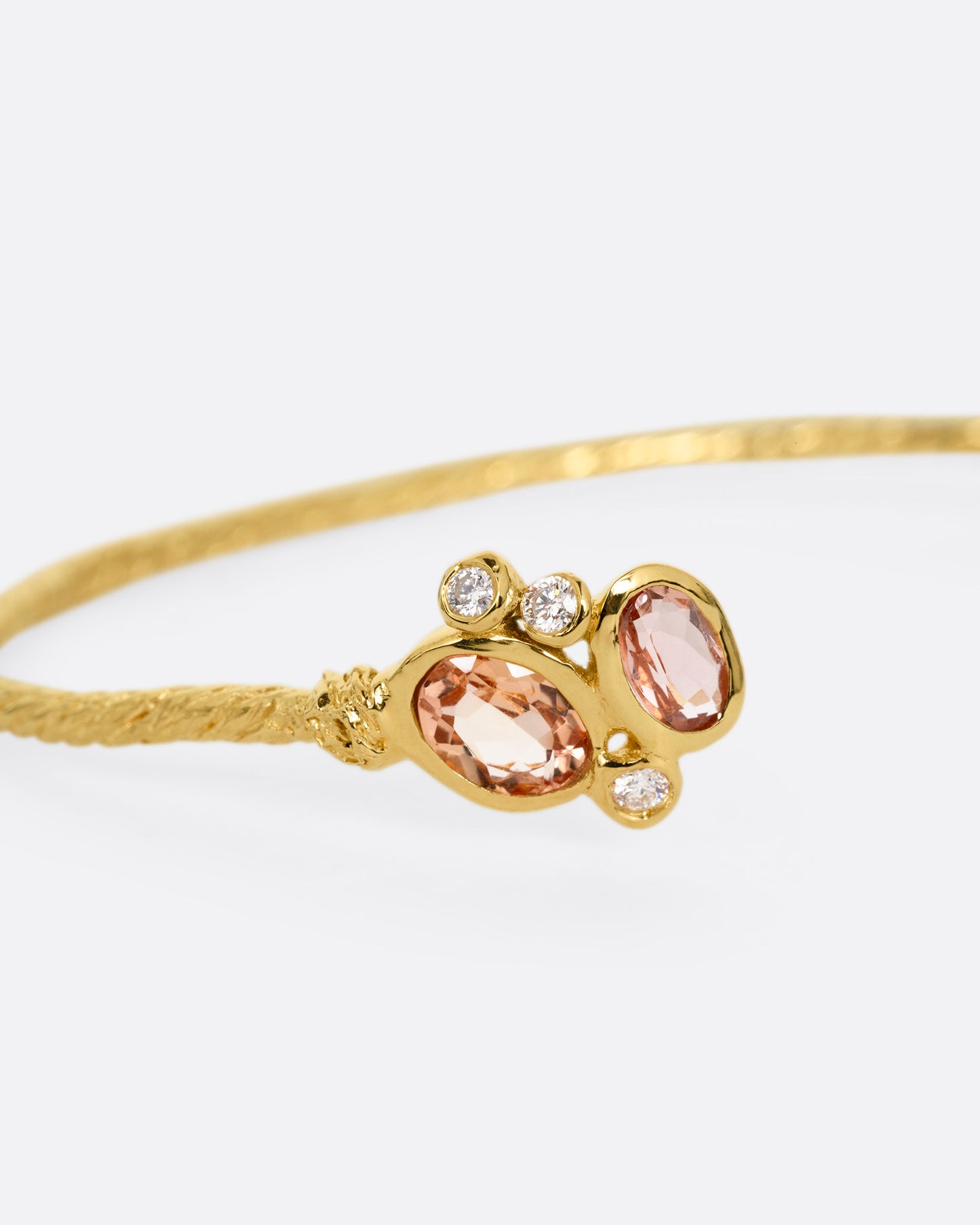 A close up of a yellow gold hand carved cuff bracelet with clusters of tourmalines and diamonds on either side of its open front.