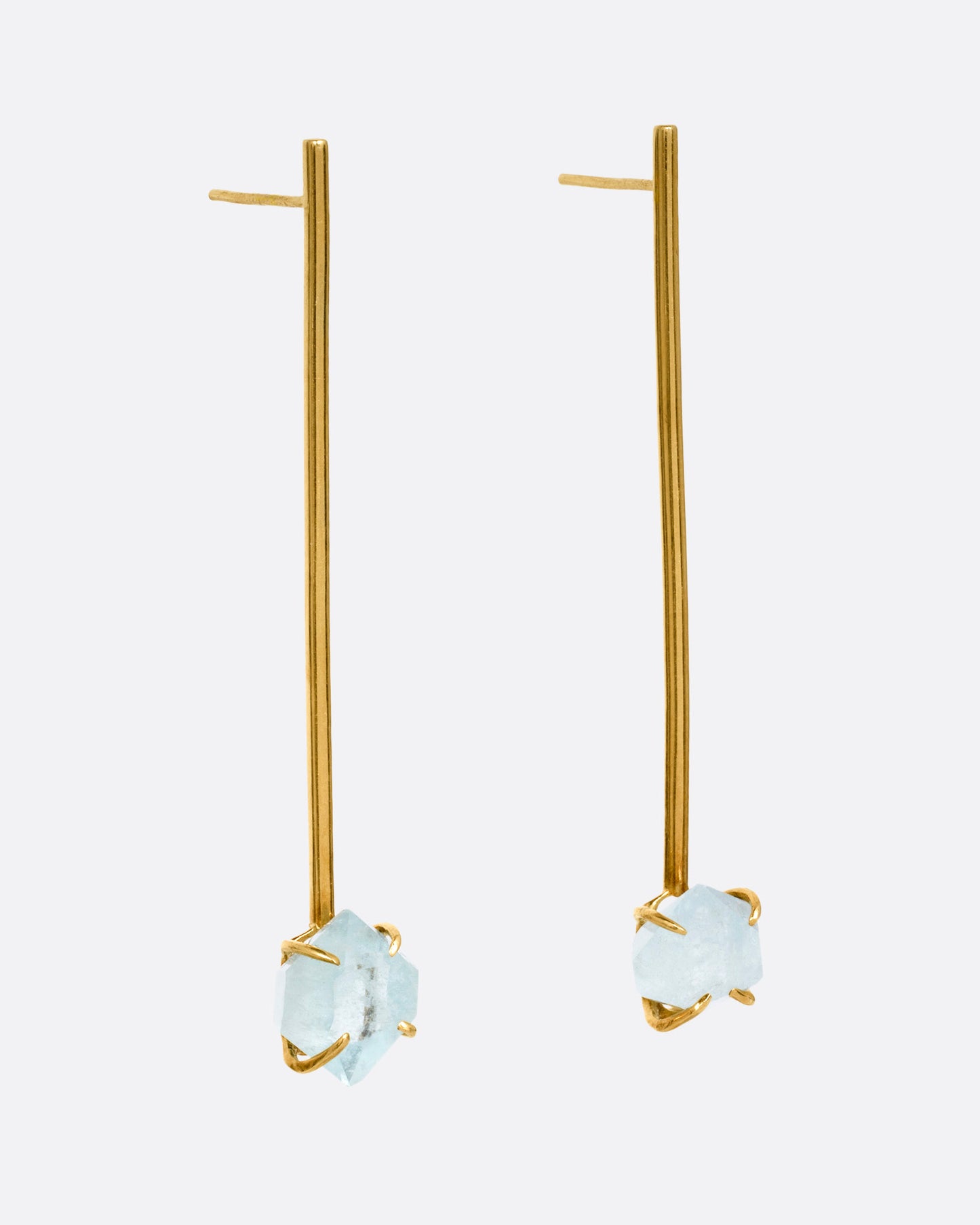 A pair of yellow gold bar earrings with  prong set uncut aquamarines at the base, shown from the side.