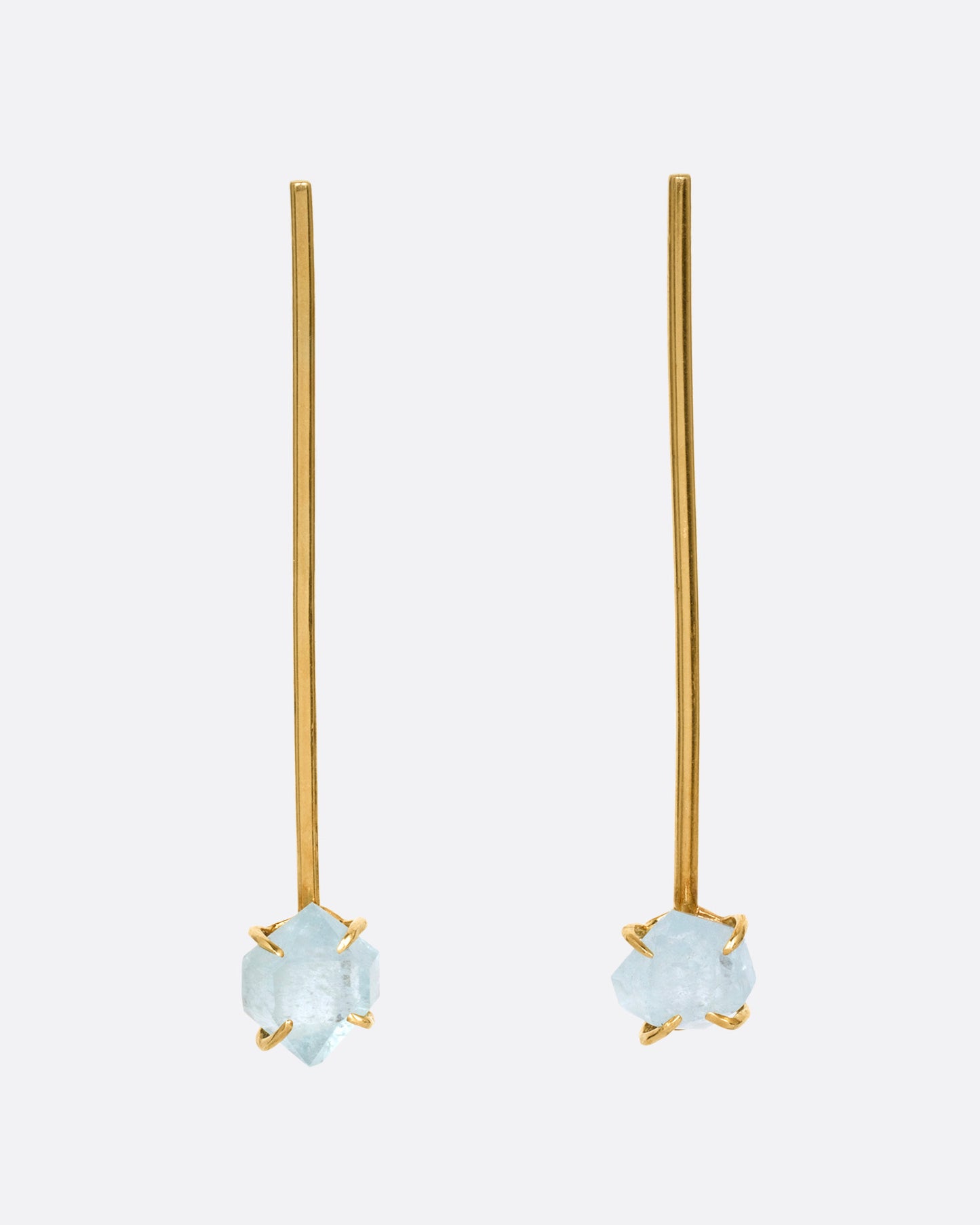 A pair of yellow gold bar earrings with  prong set uncut aquamarines at the base, shown from the front.