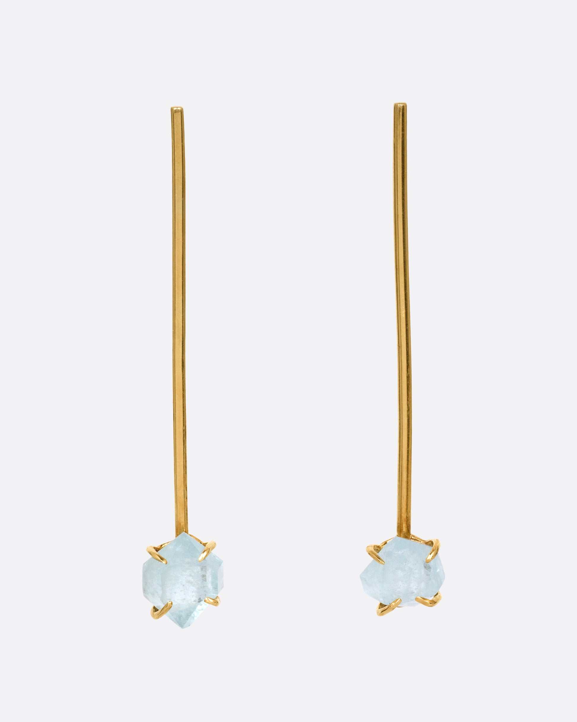 A pair of yellow gold bar earrings with  prong set uncut aquamarines at the base, shown from the front.