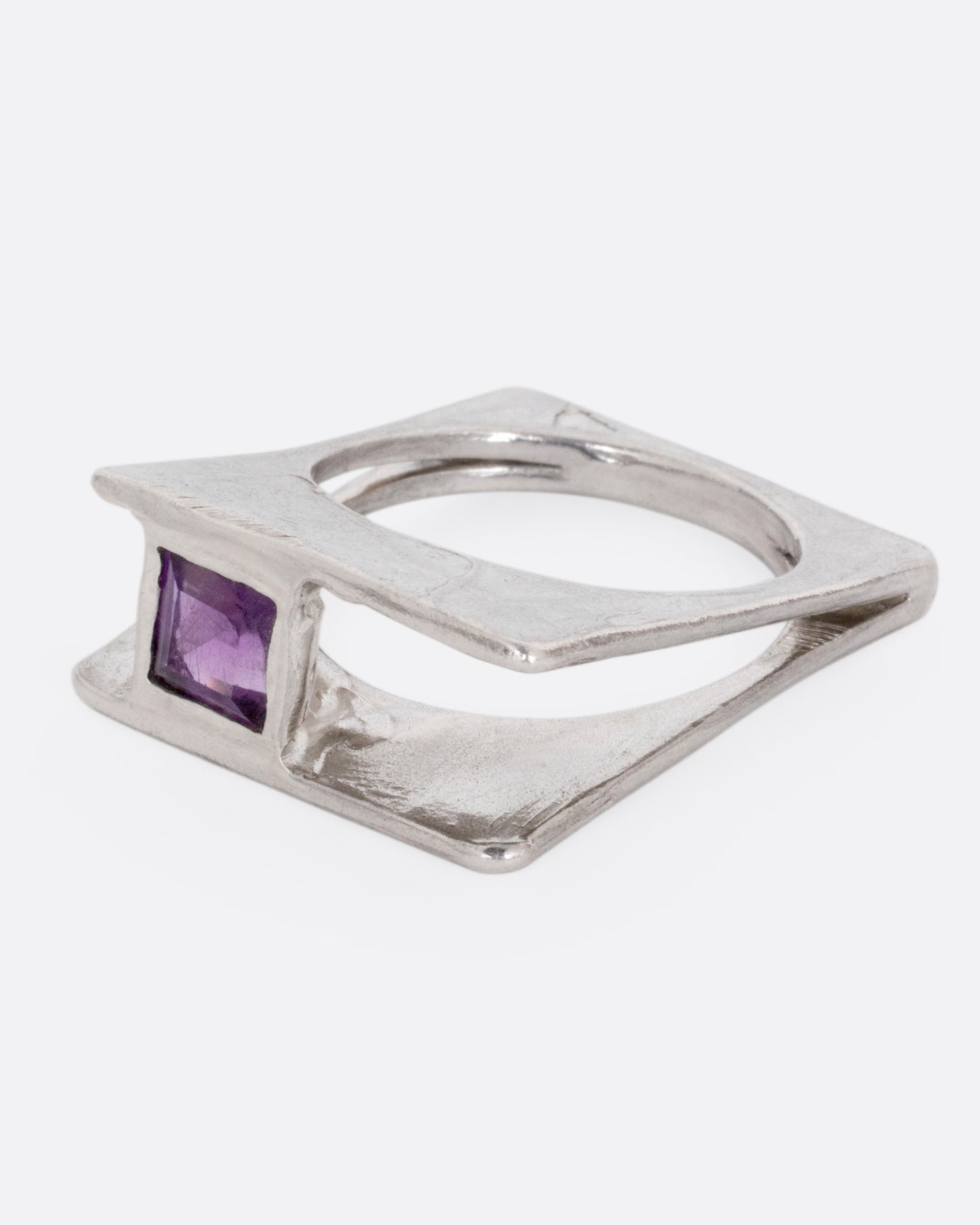 A silver square ring that widens to reveal a princess cut amethyst, shown from the side.