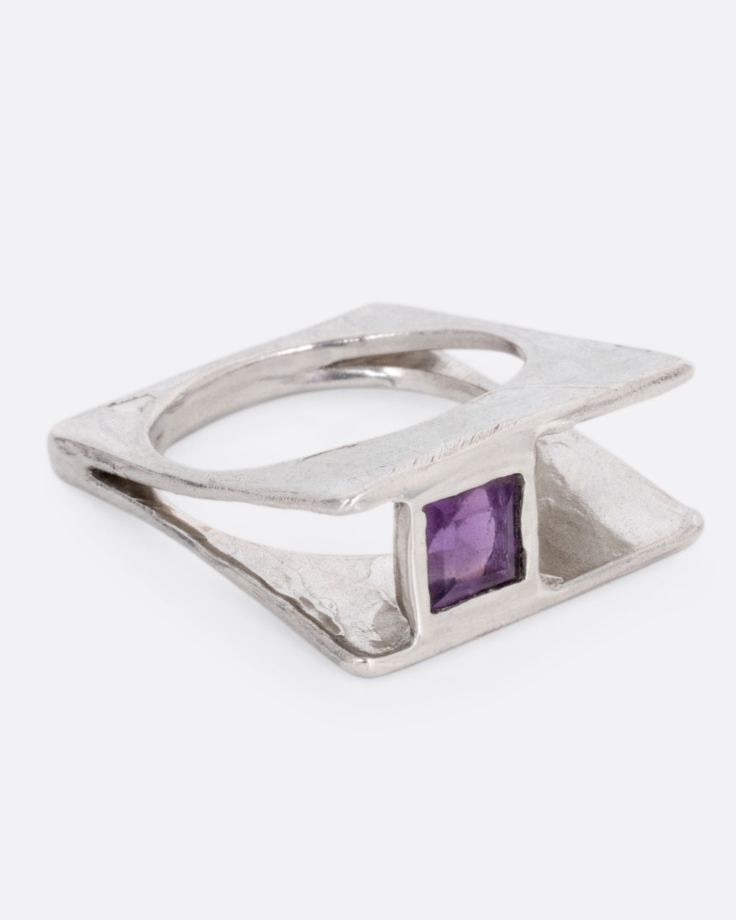 A silver square ring that widens to reveal a princess cut amethyst, shown from the side.