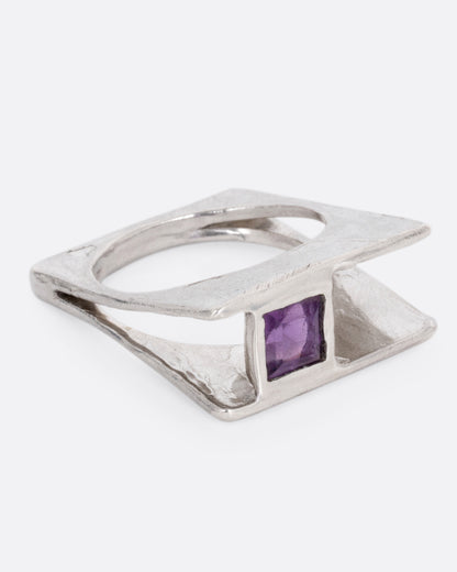 A silver square ring that widens to reveal a princess cut amethyst, shown from the side.