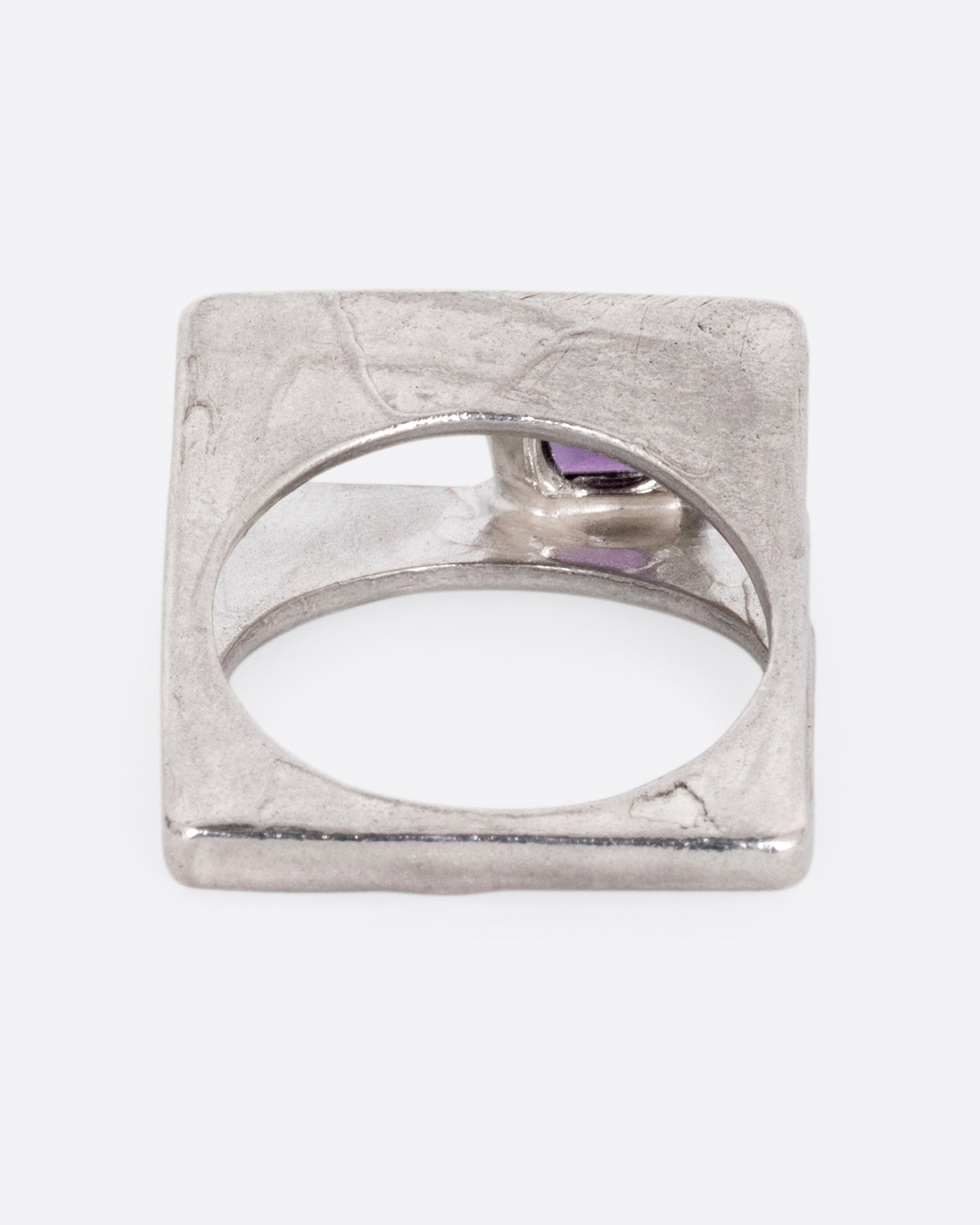 A silver square ring that widens to reveal a princess cut amethyst, shown from the back.