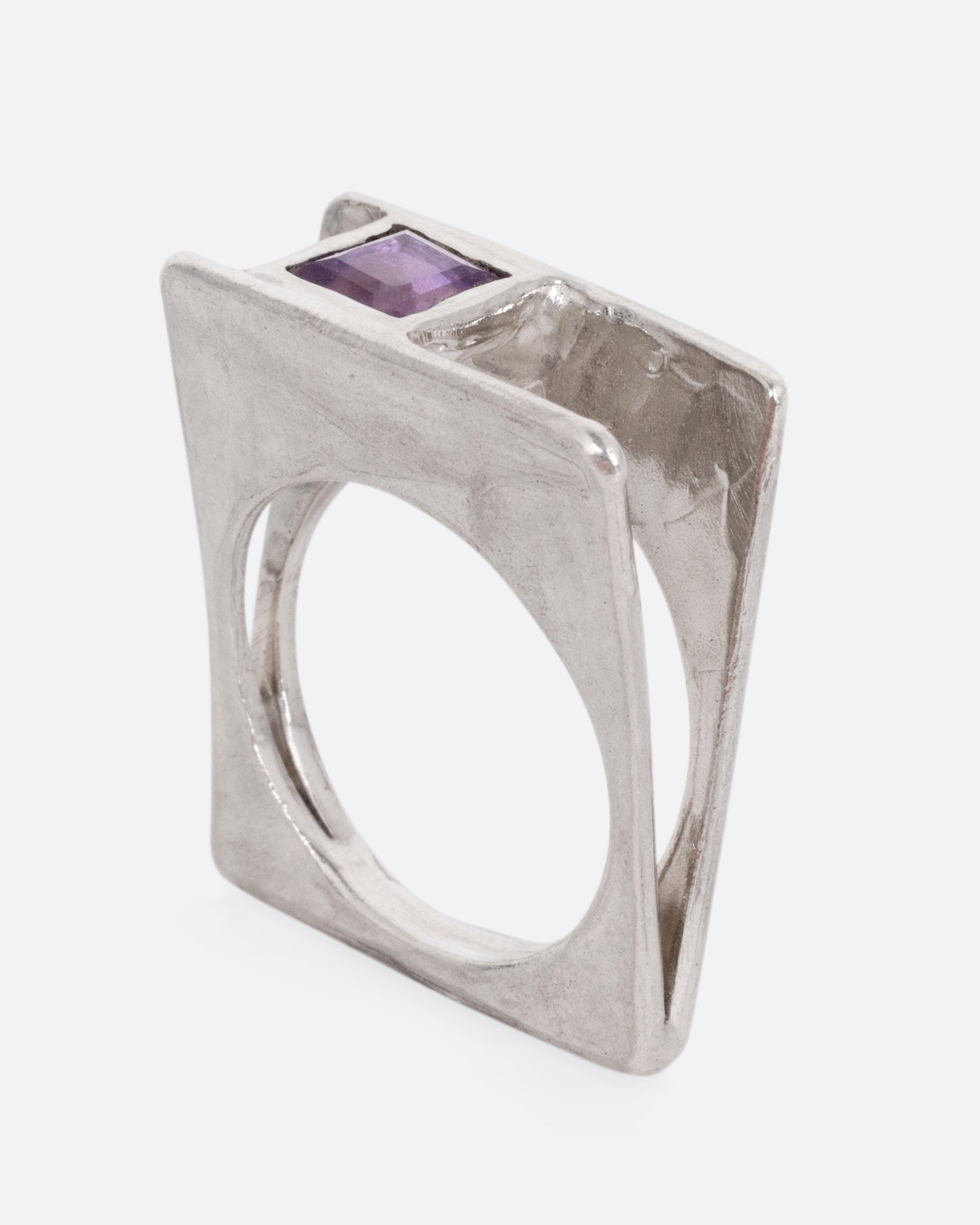 A silver square ring that widens to reveal a princess cut amethyst, shown from the side standing up.