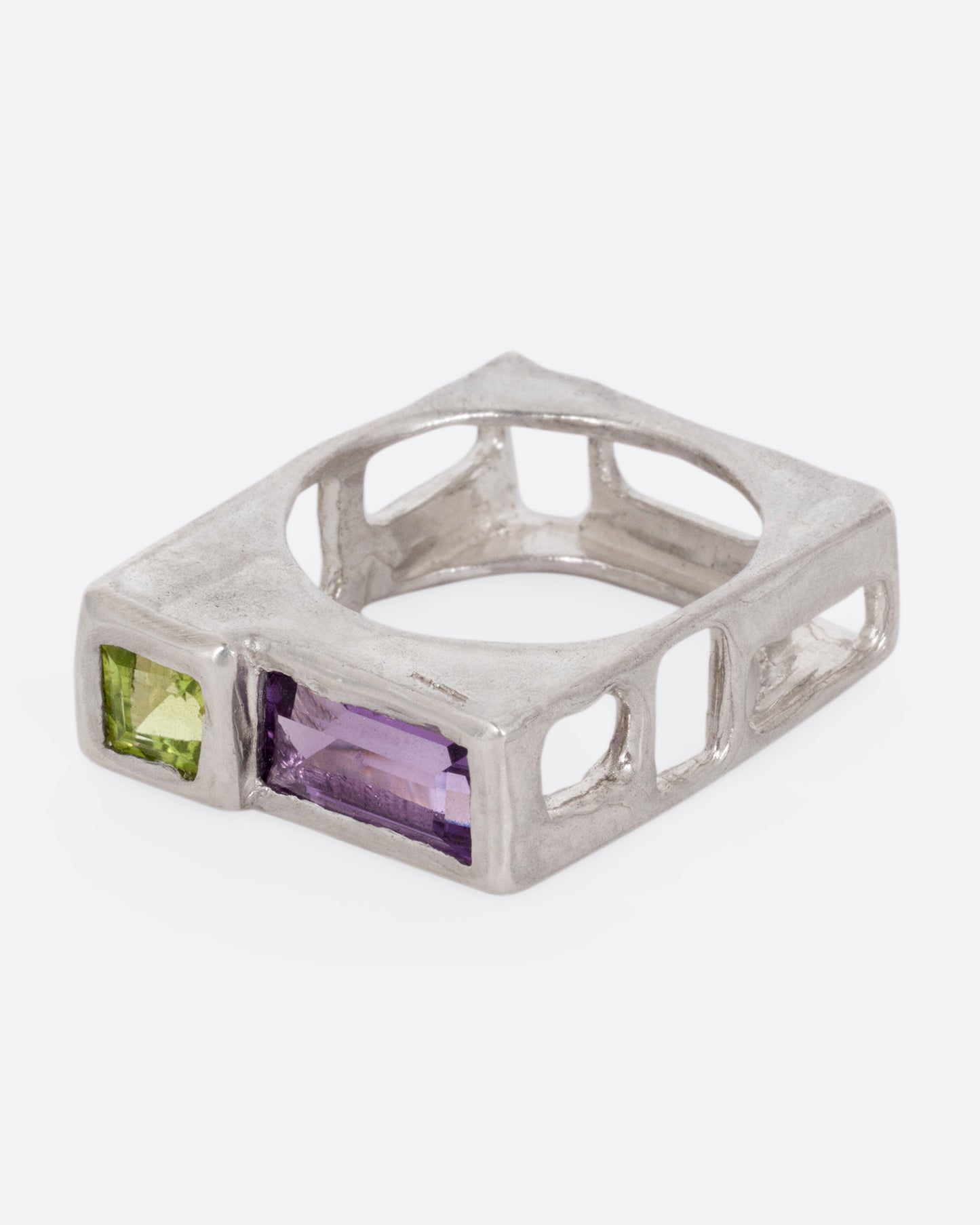 A silver square ring with a princess cut peridot and baguette amethyst, shown from the side.