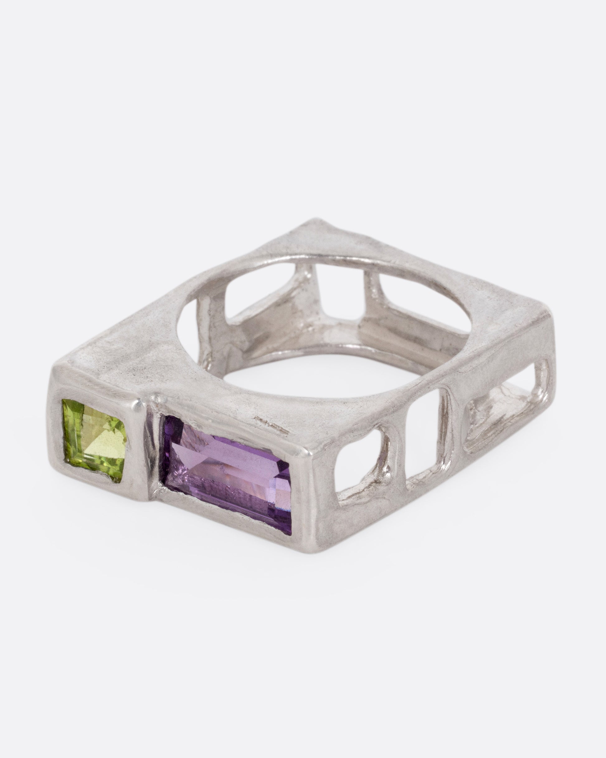 A silver square ring with a princess cut peridot and baguette amethyst, shown from the side.