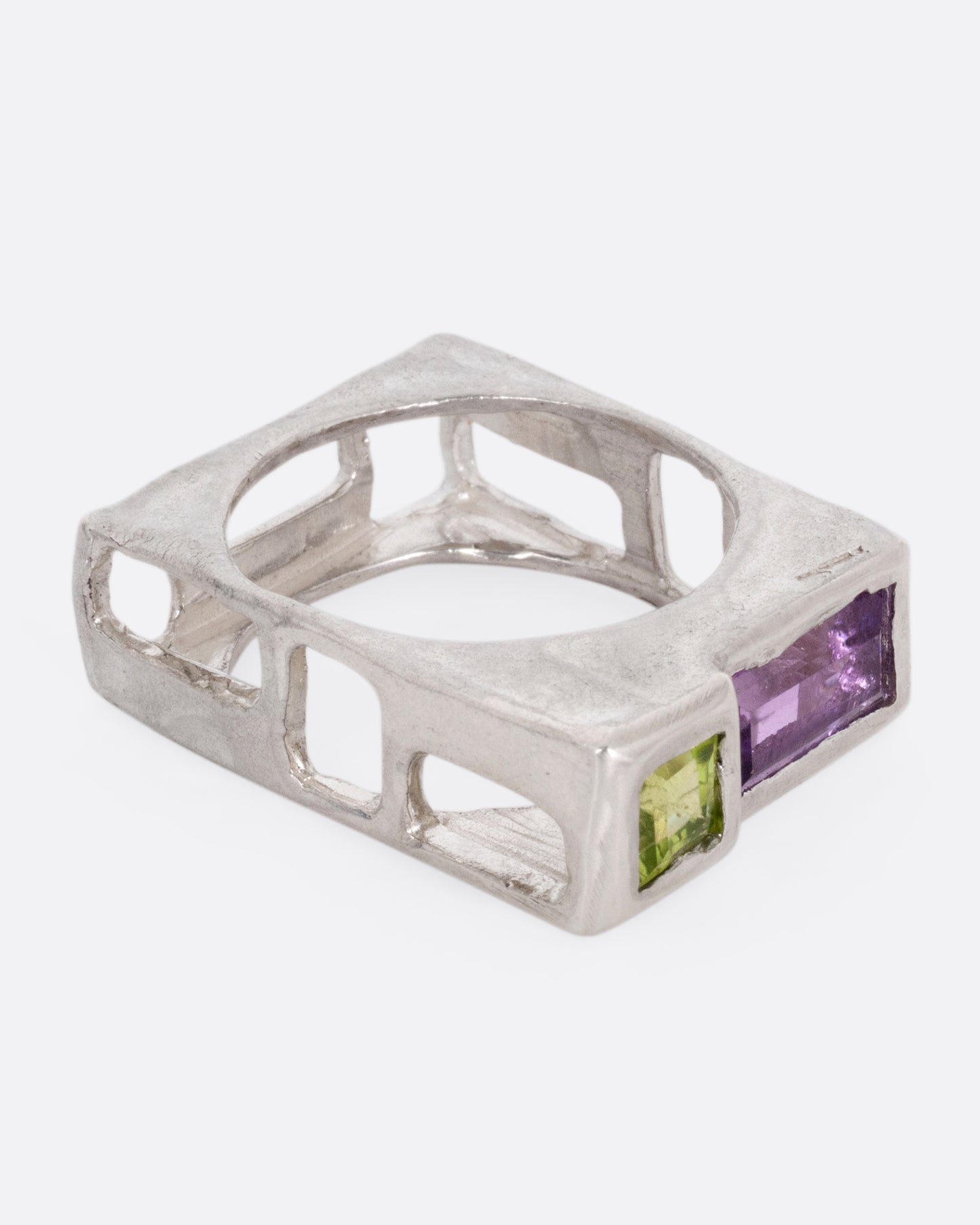 A silver square ring with a princess cut peridot and baguette amethyst, shown from the side.