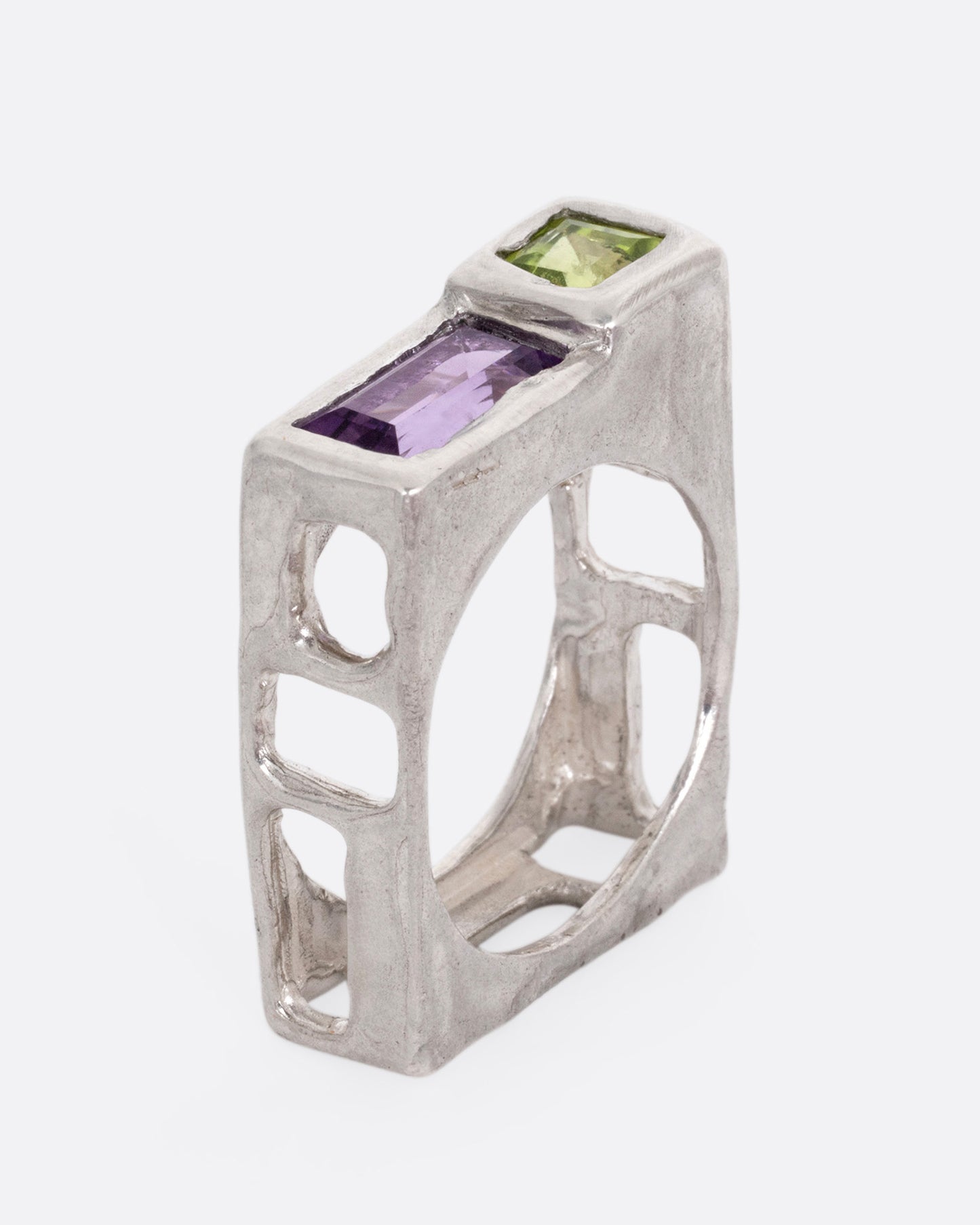 A silver square ring with a princess cut peridot and baguette amethyst, shown standing up from the side.