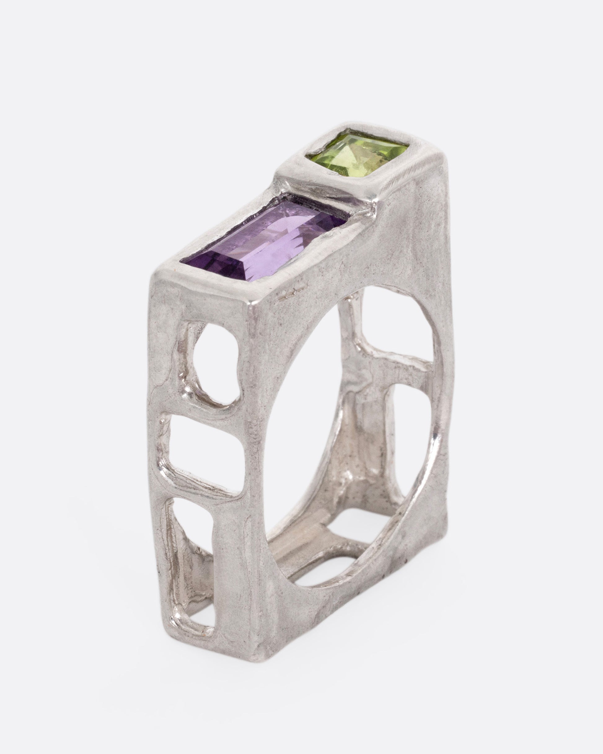 A silver square ring with a princess cut peridot and baguette amethyst, shown standing up from the side.