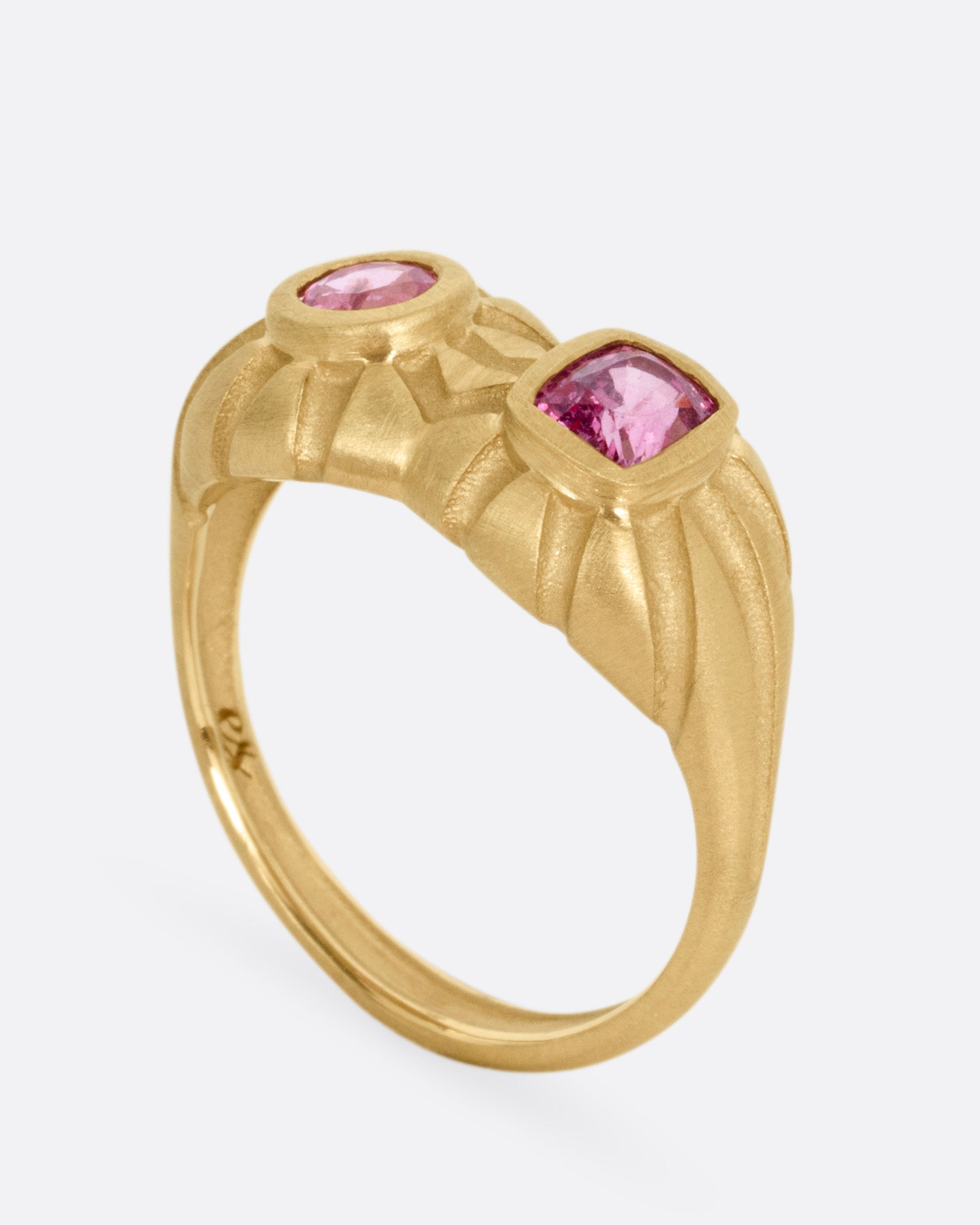 A yellow gold dimensional domed ring with two pink spinels, one round and one cushion cut, shown from the side standing up.