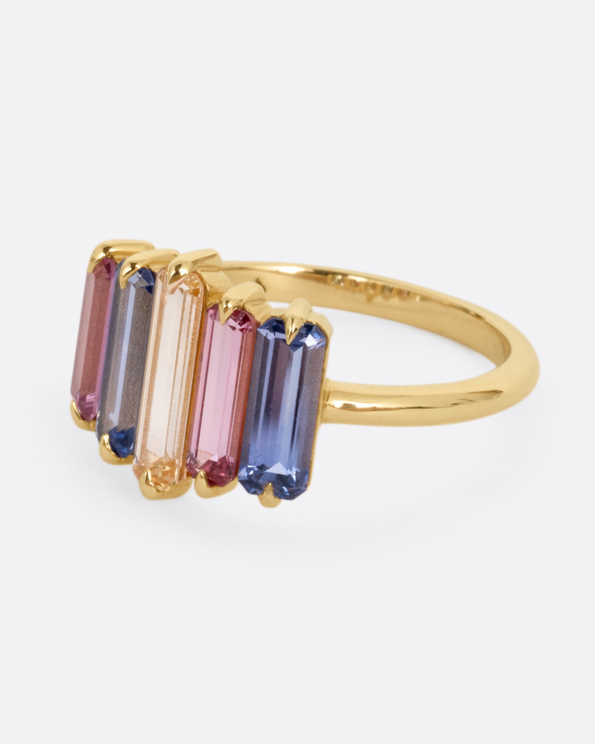 A yellow gold queue of pastel colored sapphire baguettes, shown from the side.
