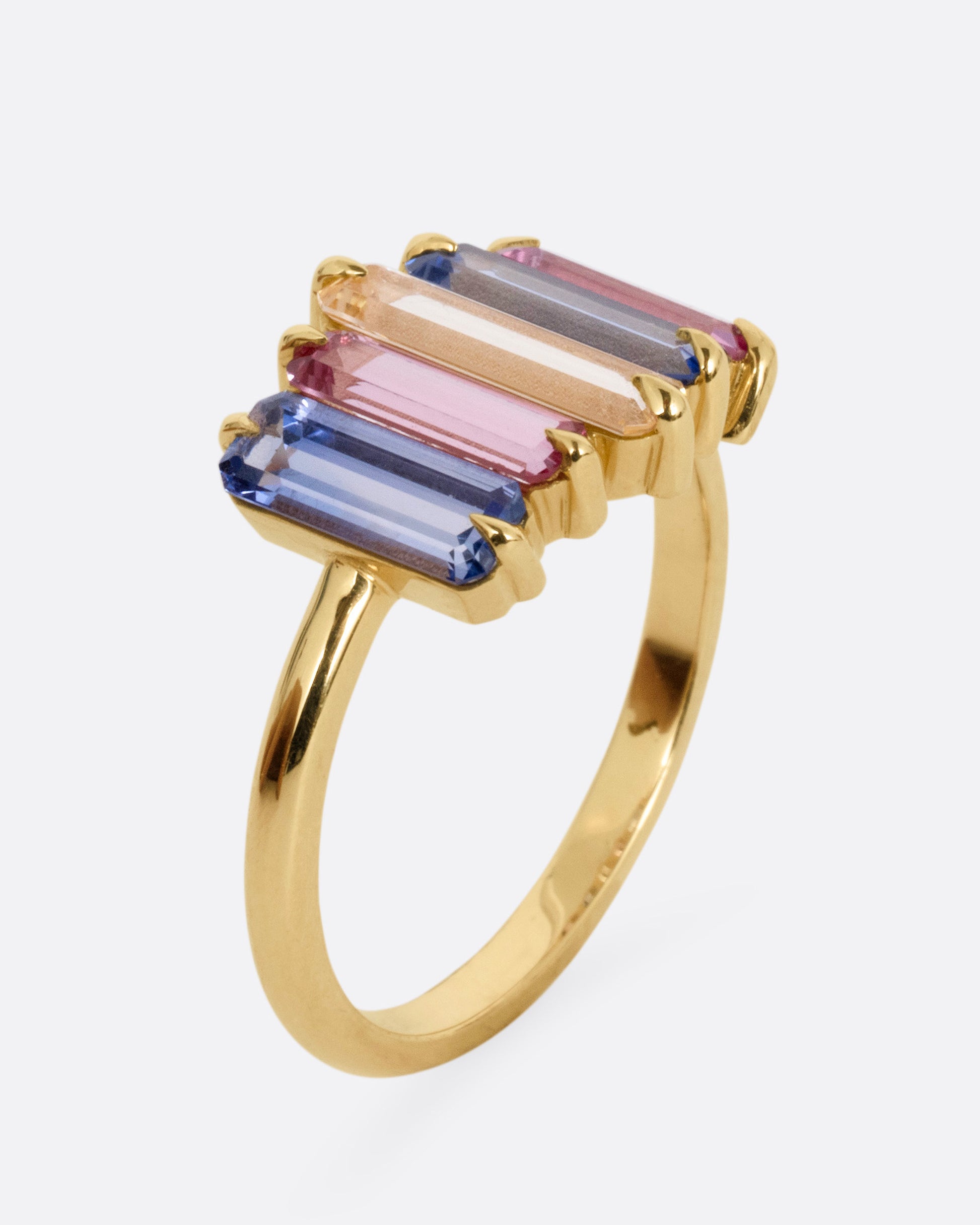 A yellow gold queue of pastel colored sapphire baguettes, shown from the side standing up.