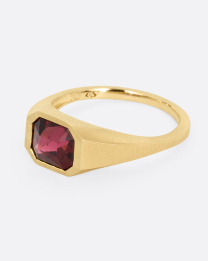 A yellow gold signet ring with a garnet, shown from the side.