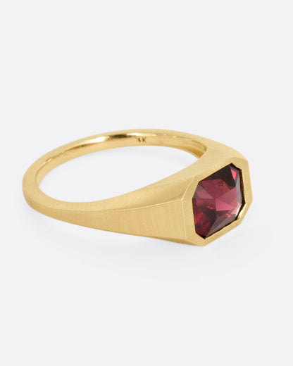 A yellow gold signet ring with a garnet, shown from the side.