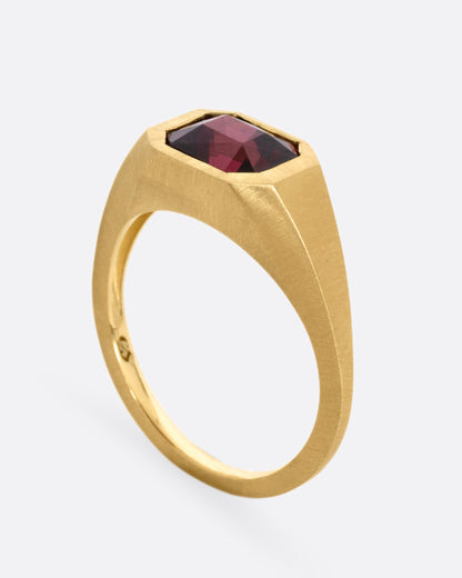 A yellow gold signet ring with a garnet, shown standing up from the side.