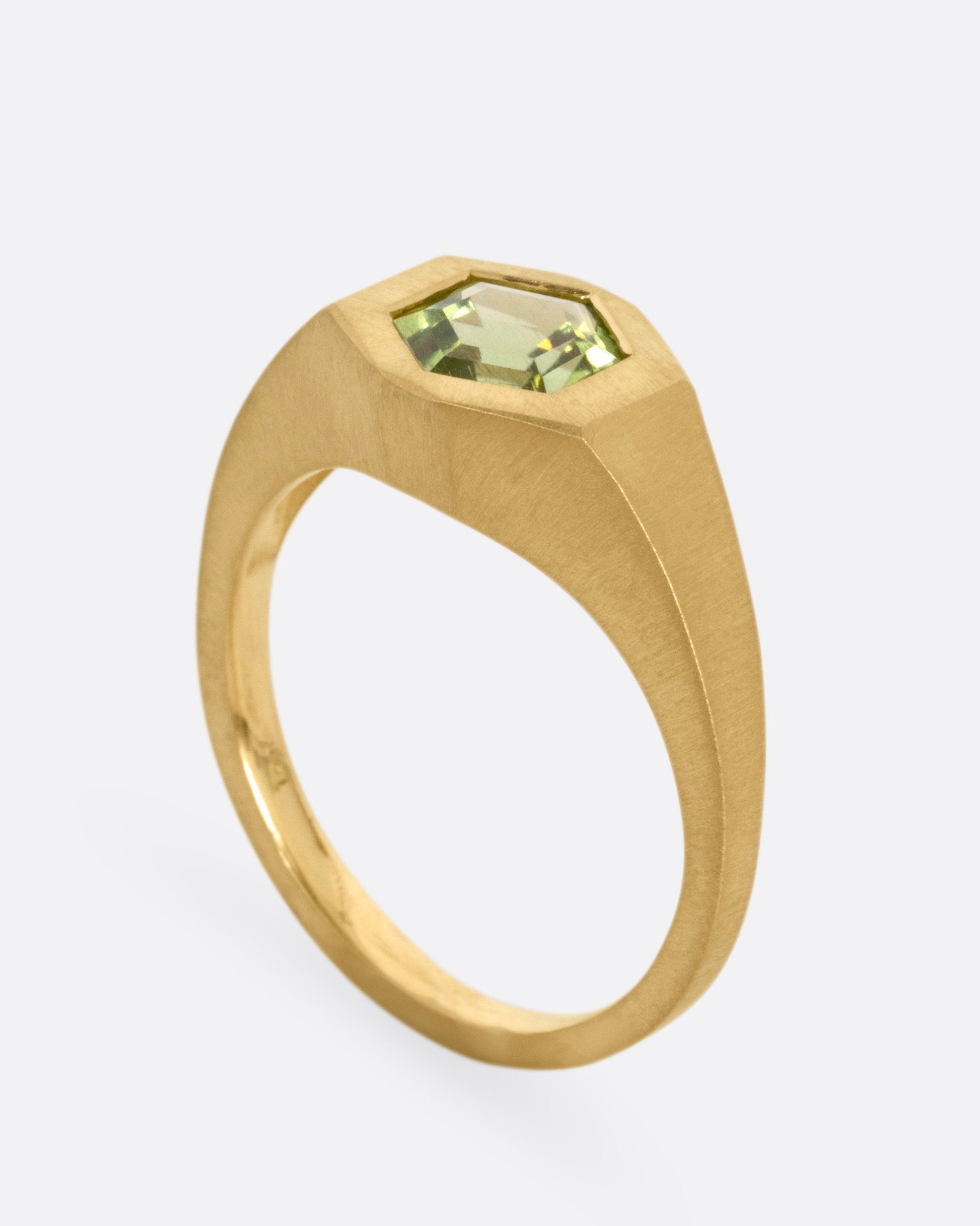 A yellow gold ring with a green hexagonal tourmaline, shown standing up from the side.