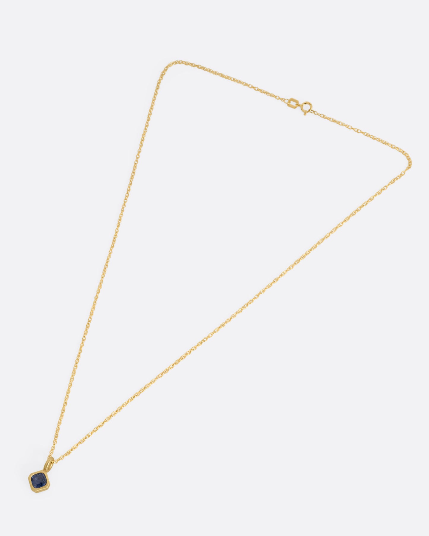 A yellow gold necklace with a cushion cut sapphire pendant, shown from the front.
