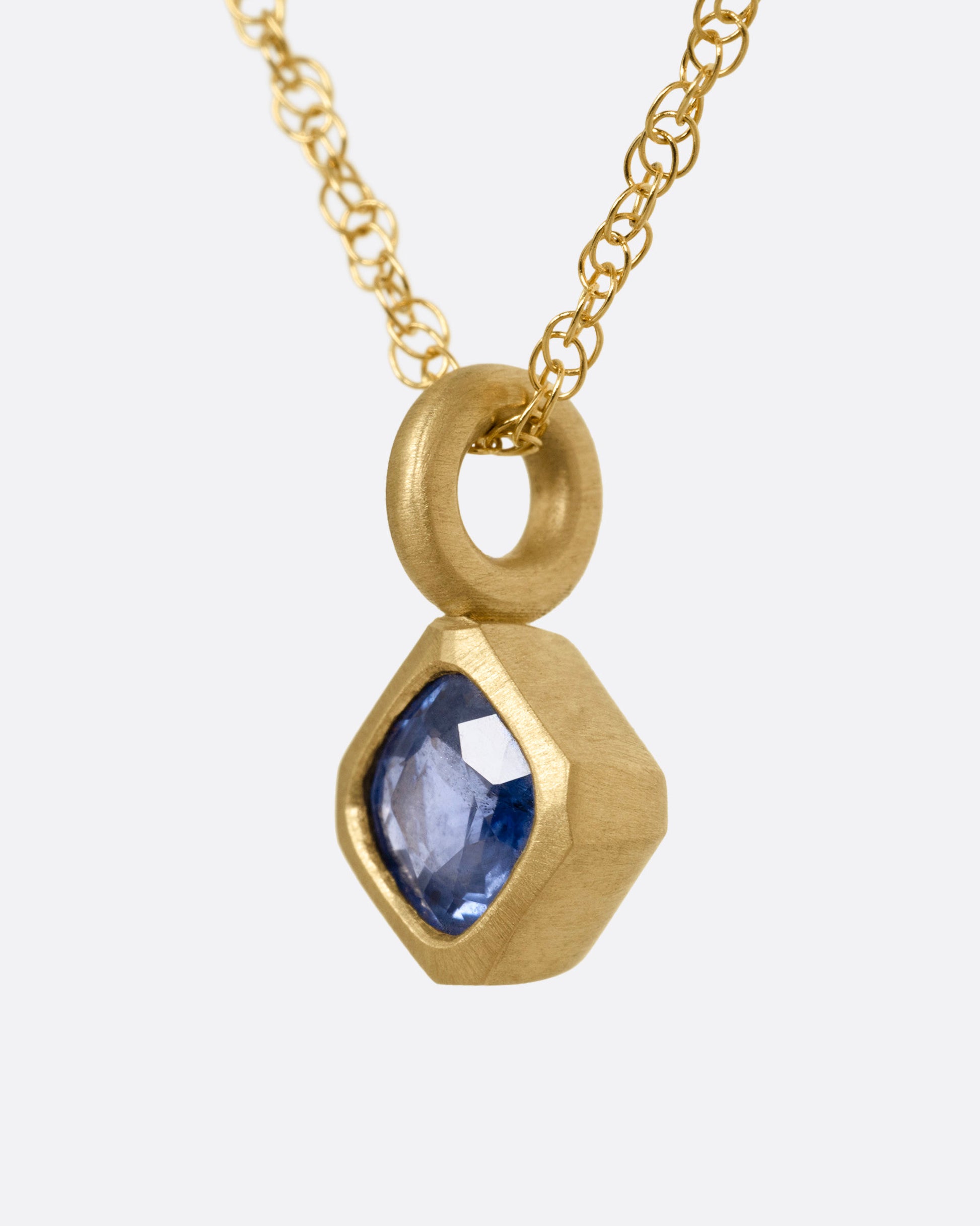 A yellow gold necklace with a cushion cut sapphire pendant, shown from the side.