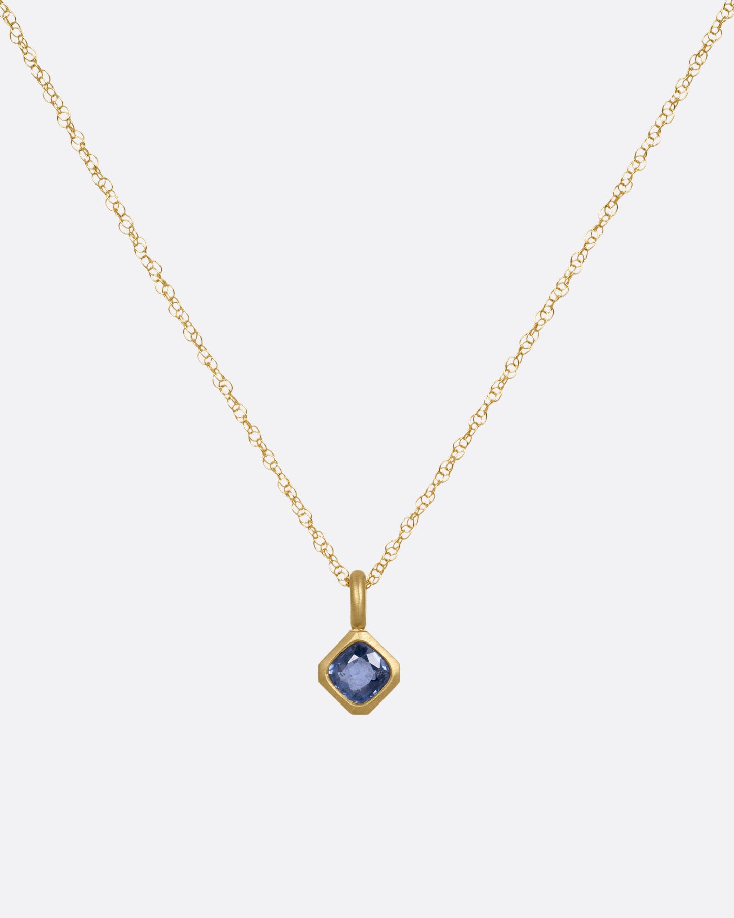 A yellow gold necklace with a cushion cut sapphire pendant, shown from the front.