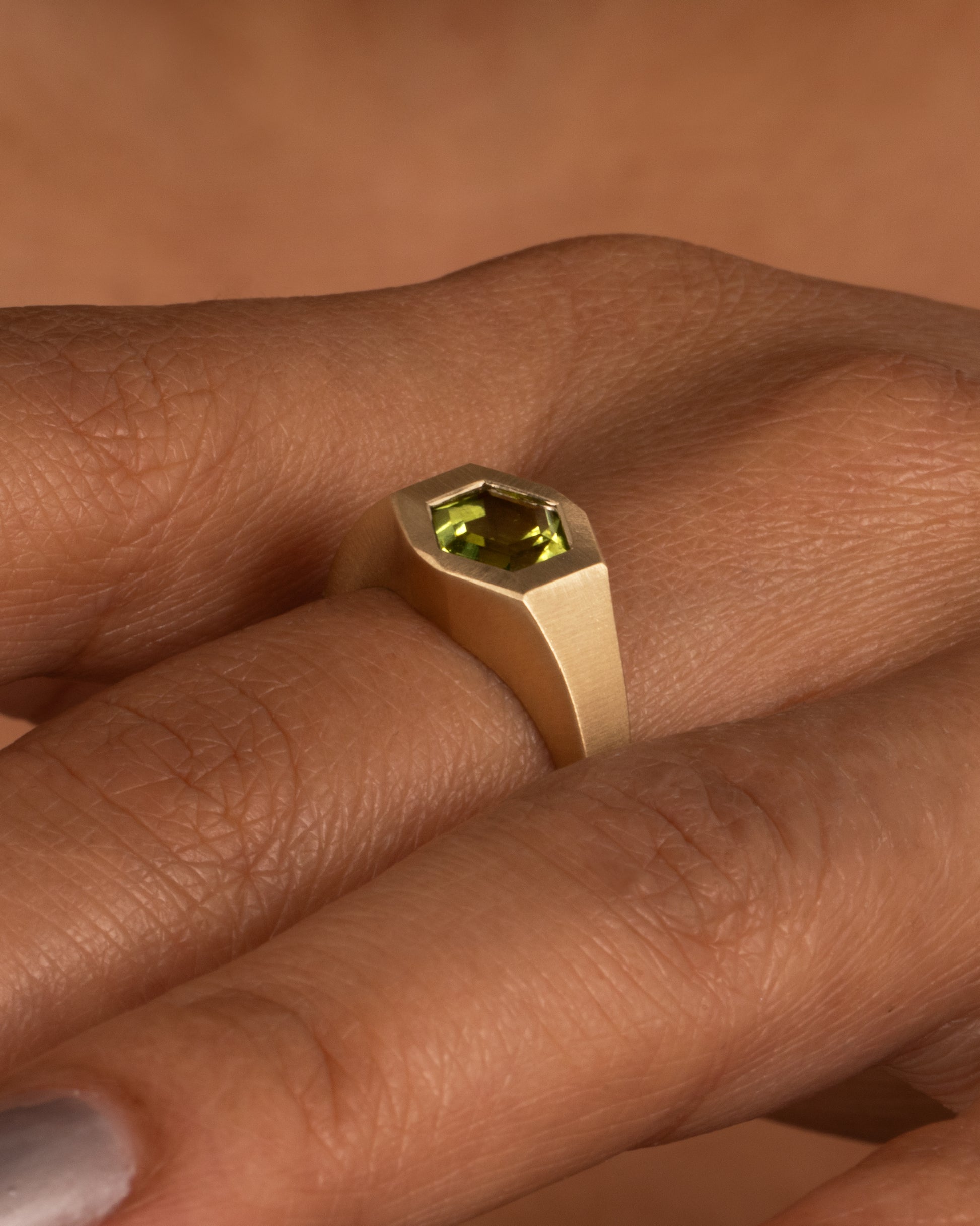 A yellow gold ring with a green hexagonal tourmaline, shown on a hand.