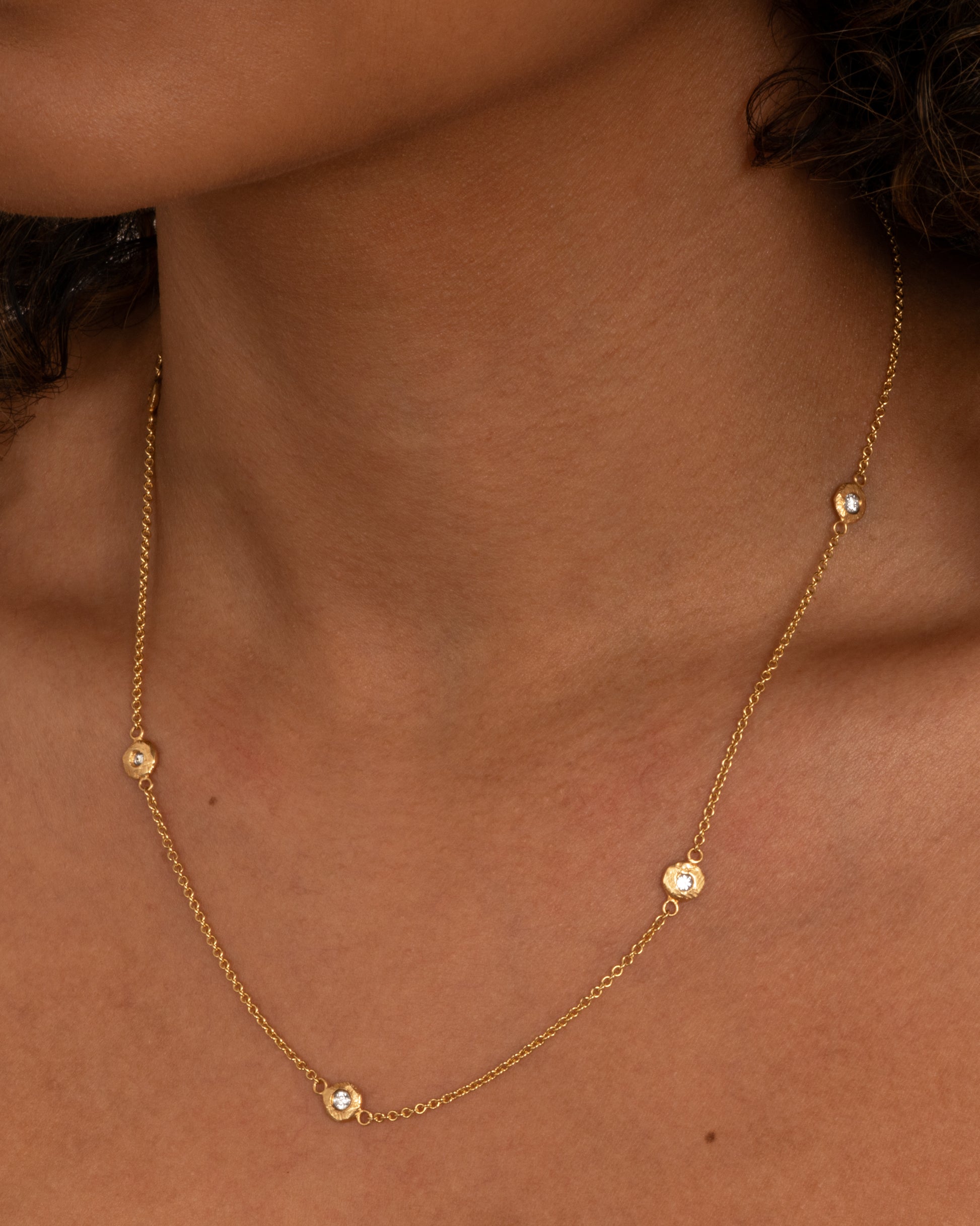 A yellow gold cable chain necklace with five diamonds set in hand carved bezels. Shown worn around the neck.