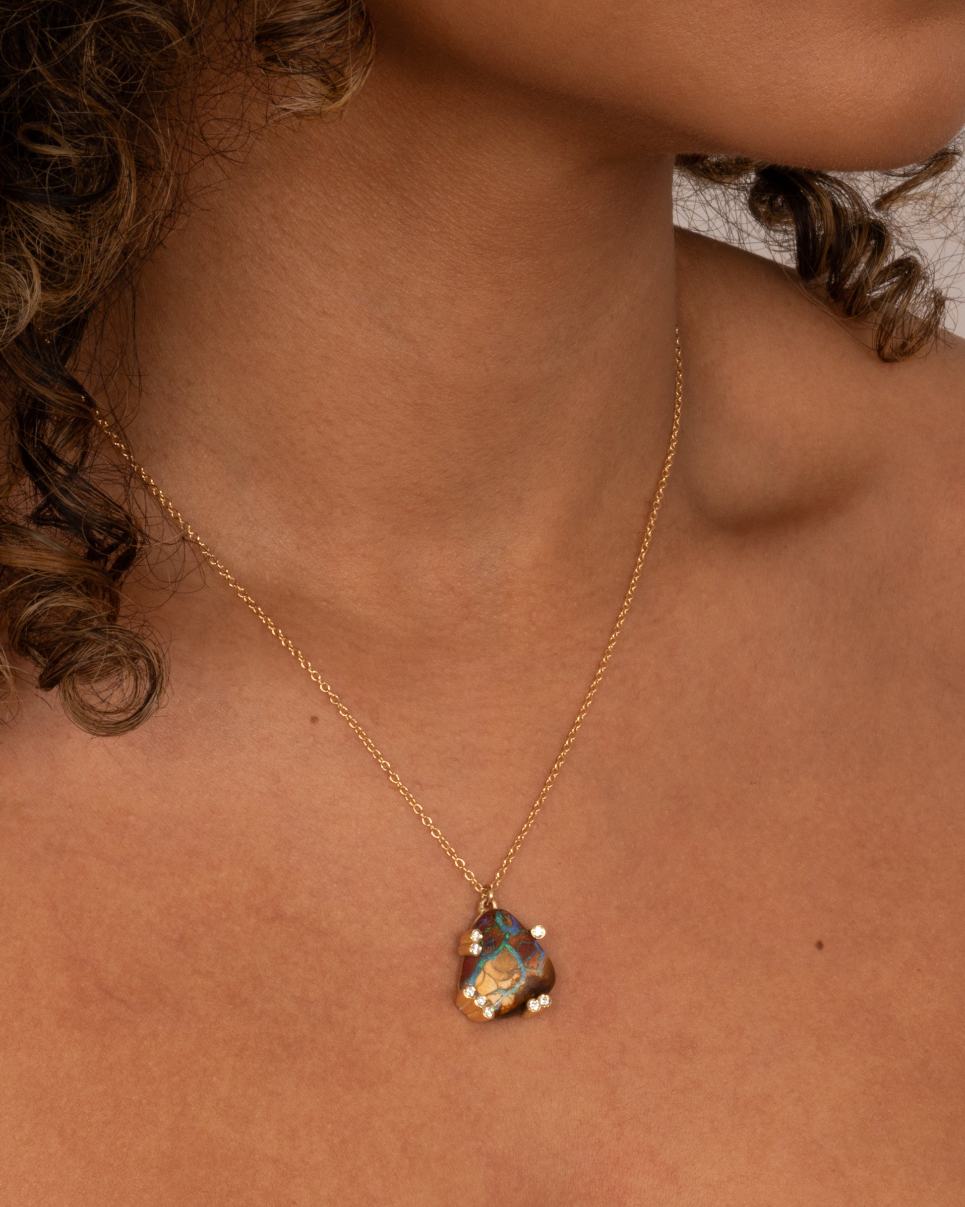 A yellow gold cable chain necklace with a free-form boulder opal and diamond anemones. Shown worn around the neck.