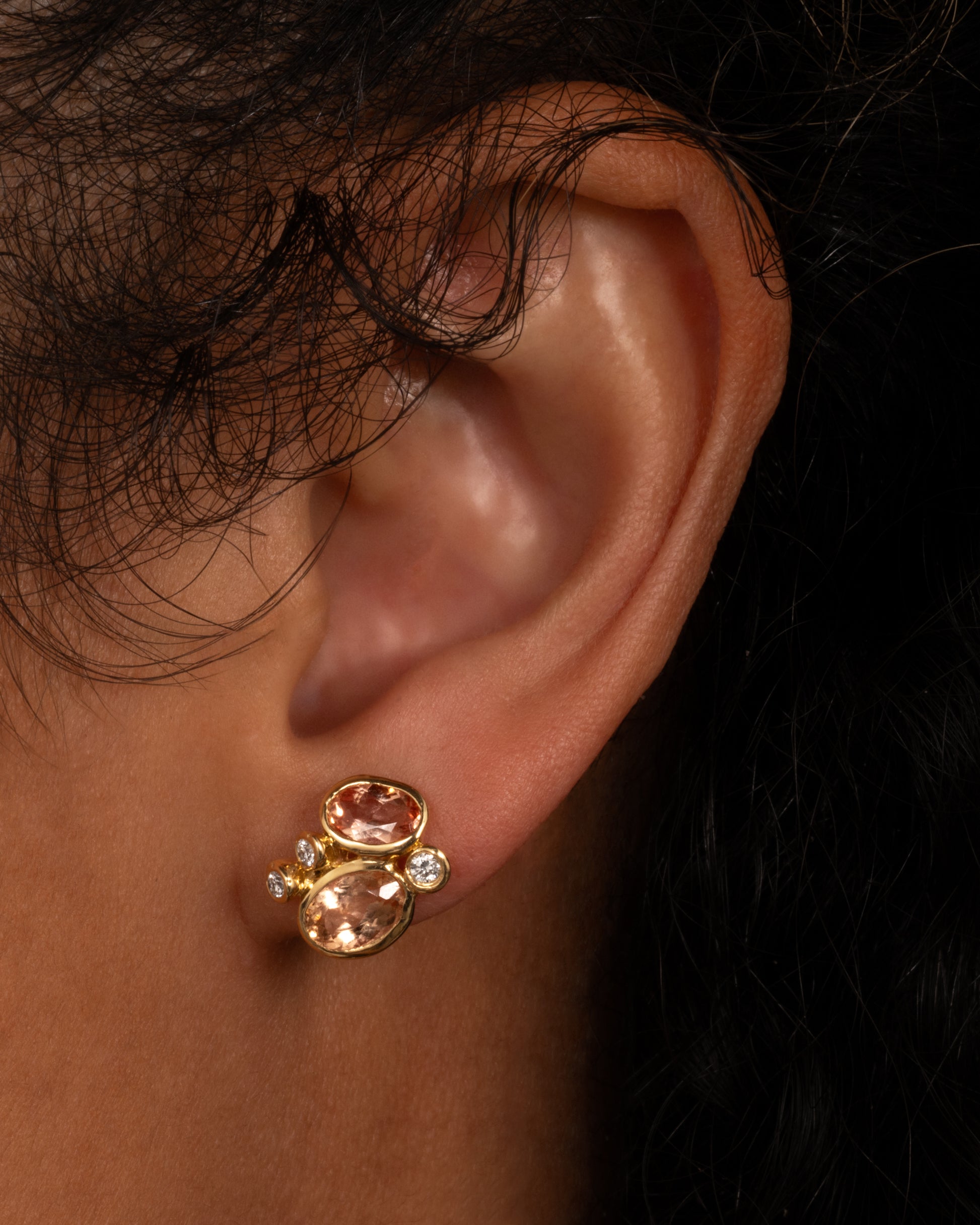 A yellow gold stud earring with a cluster of pink tourmalines and white diamonds, shown on a person.