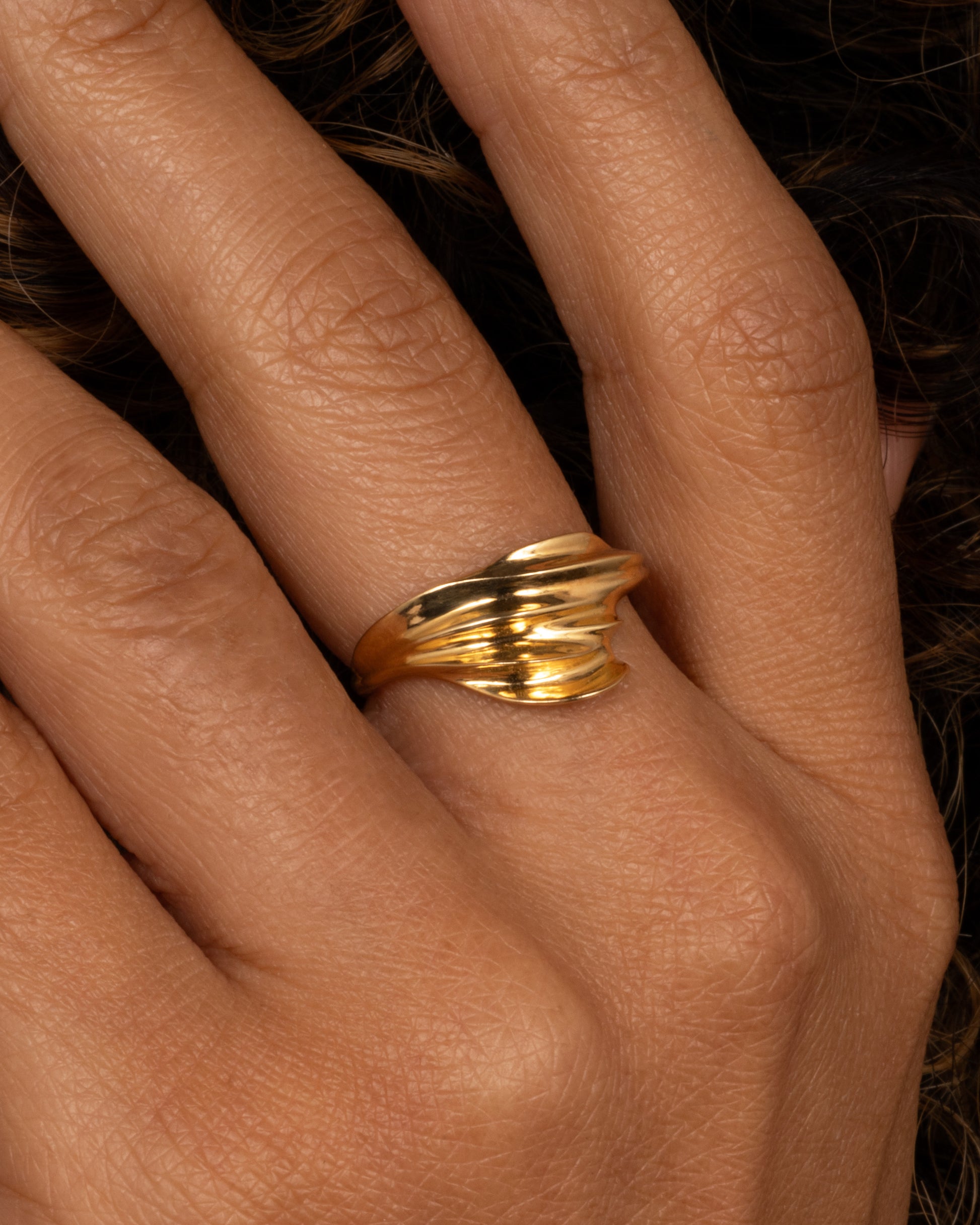 A yellow gold ring with a fluid, dimensional silhouette and narrow back, shown from the front on a hand.
