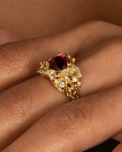 A yellow gold ring with a bed of diamond tipped anemones, and a red rubellite, shown on a hand from the side.