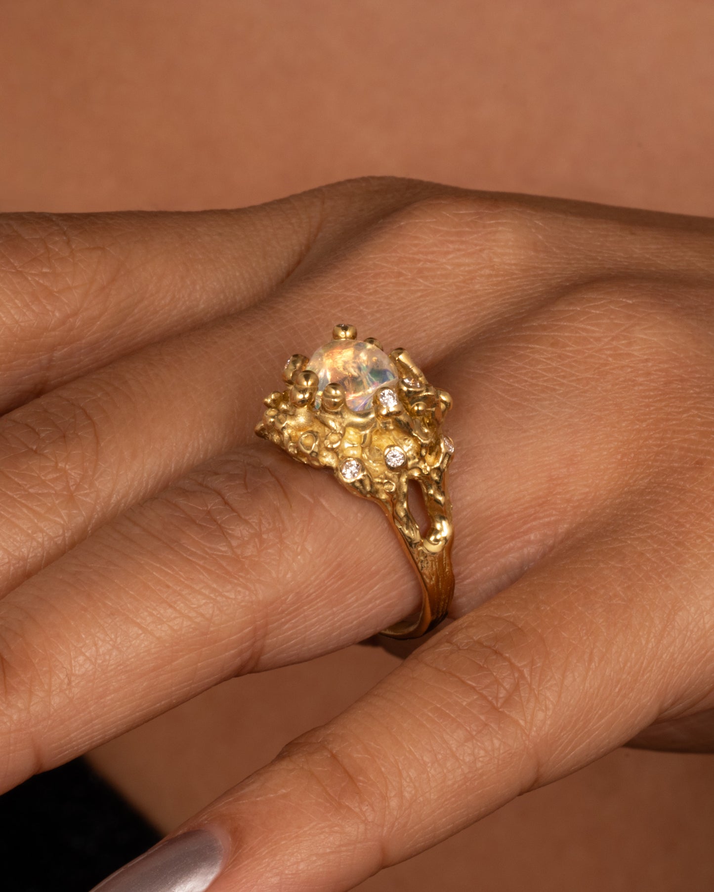 A yellow gold ring with a dimensional nest-like setting studded with diamonds and an opal, shown from the side on a hand.