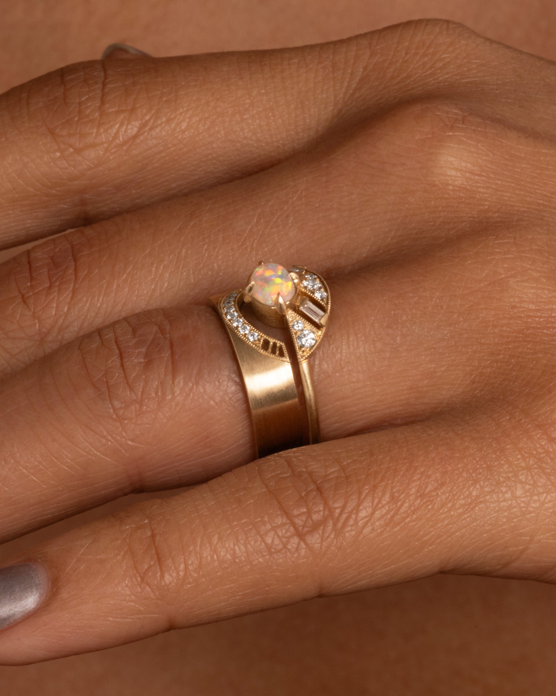 A yellow gold arched ring with eight bead set diamonds set above the half moon cutout at the center, shown on a hand stacked with an opal and diamond ring.