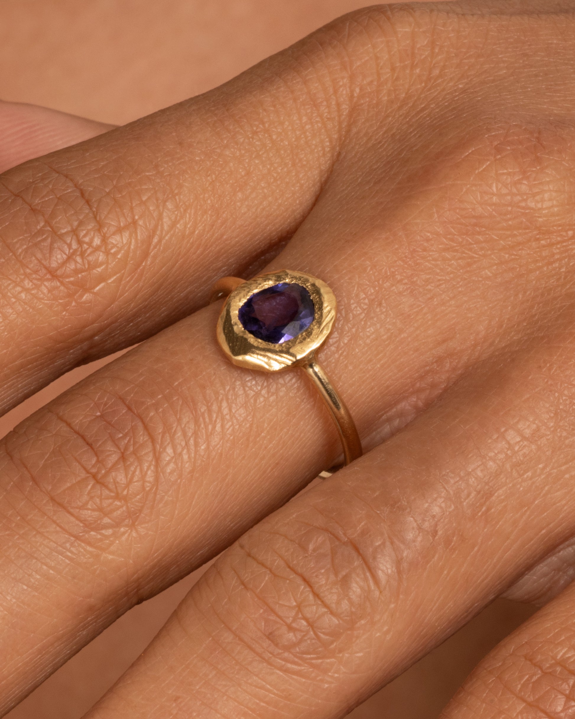 A yellow gold ring with a purple blue sapphire, shown worn on a finger.