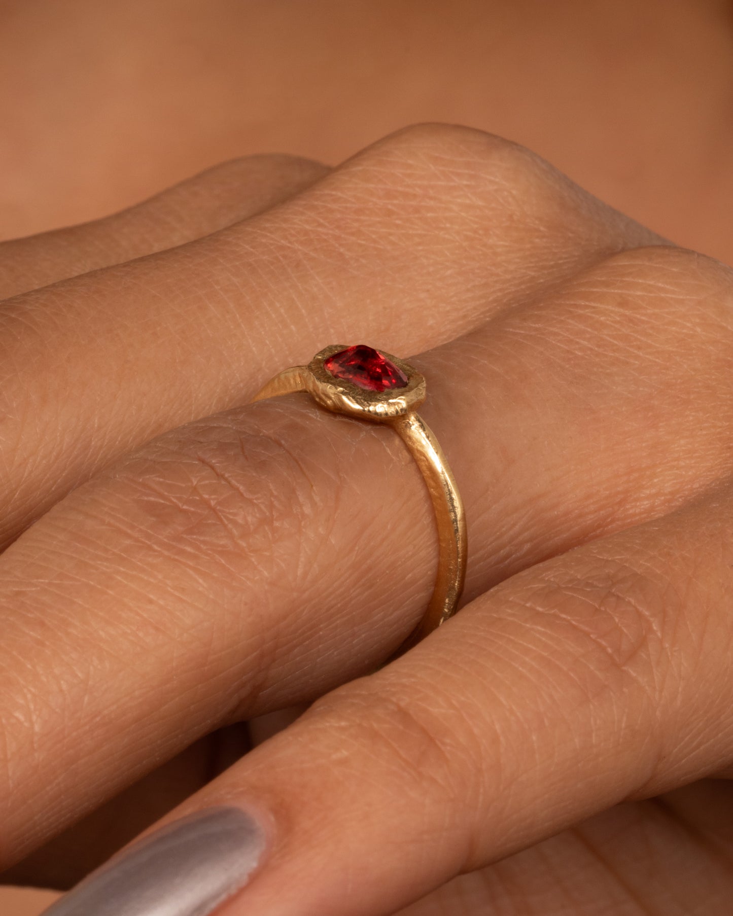 A yellow gold ring with a poppy red sapphire bezel set in a hand carved band. Shown worn on a finger.