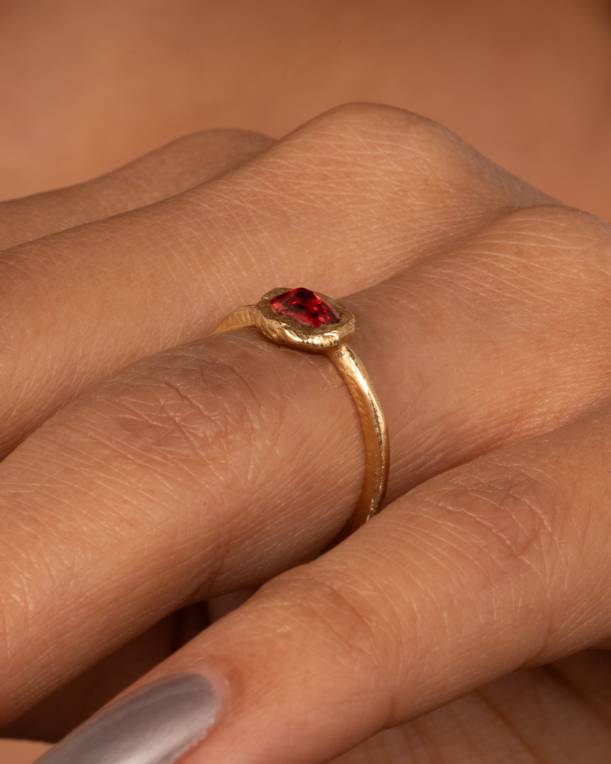 A yellow gold ring with a poppy red sapphire bezel set in a hand carved band. Shown worn on a finger.