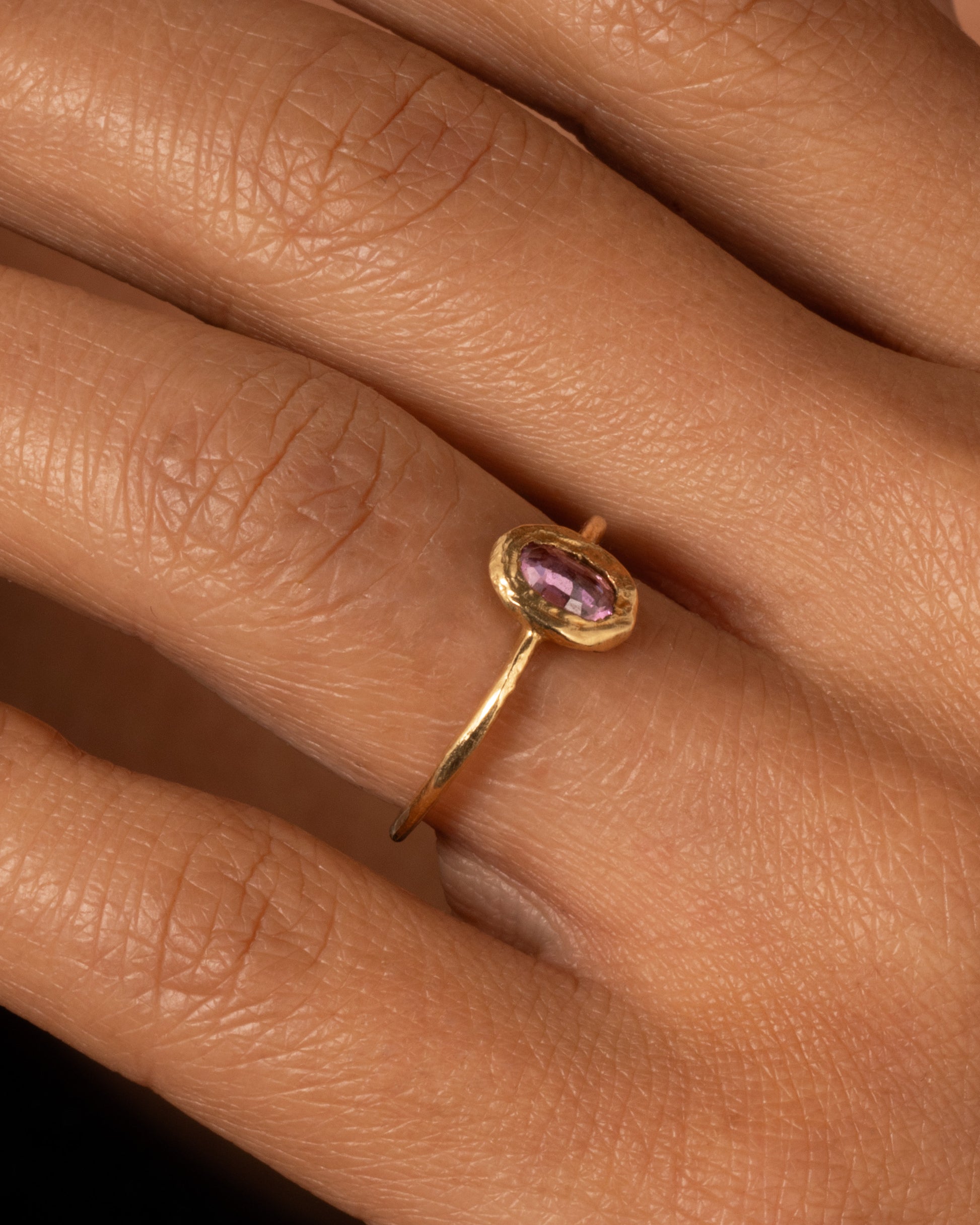 A yellow gold ring with a  pale pink sapphire in a hand carved bezel. Shown worn on a finger.