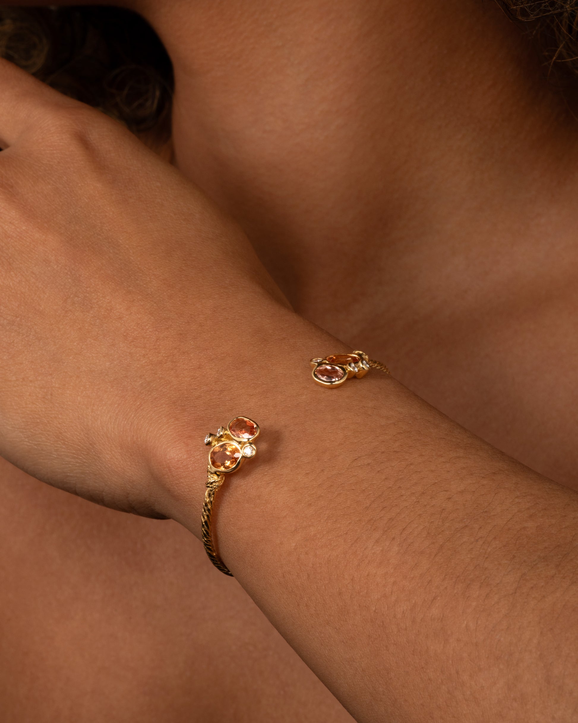 A yellow gold hand carved cuff bracelet with clusters of tourmalines and diamonds on either side of its open front, shown on a person.