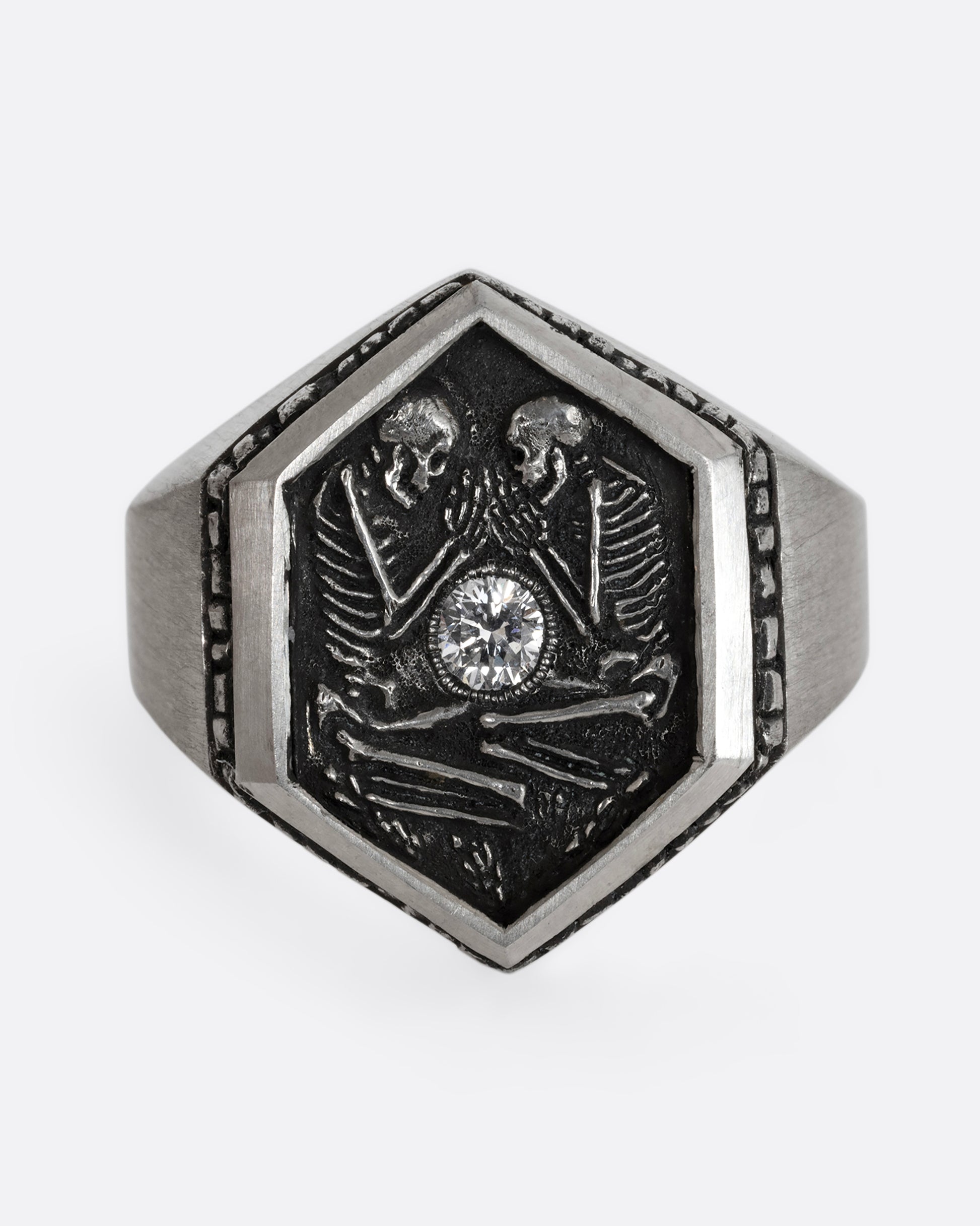 Sterling silver signet ring with two skeletons and a diamond at the center. Shown from the front.