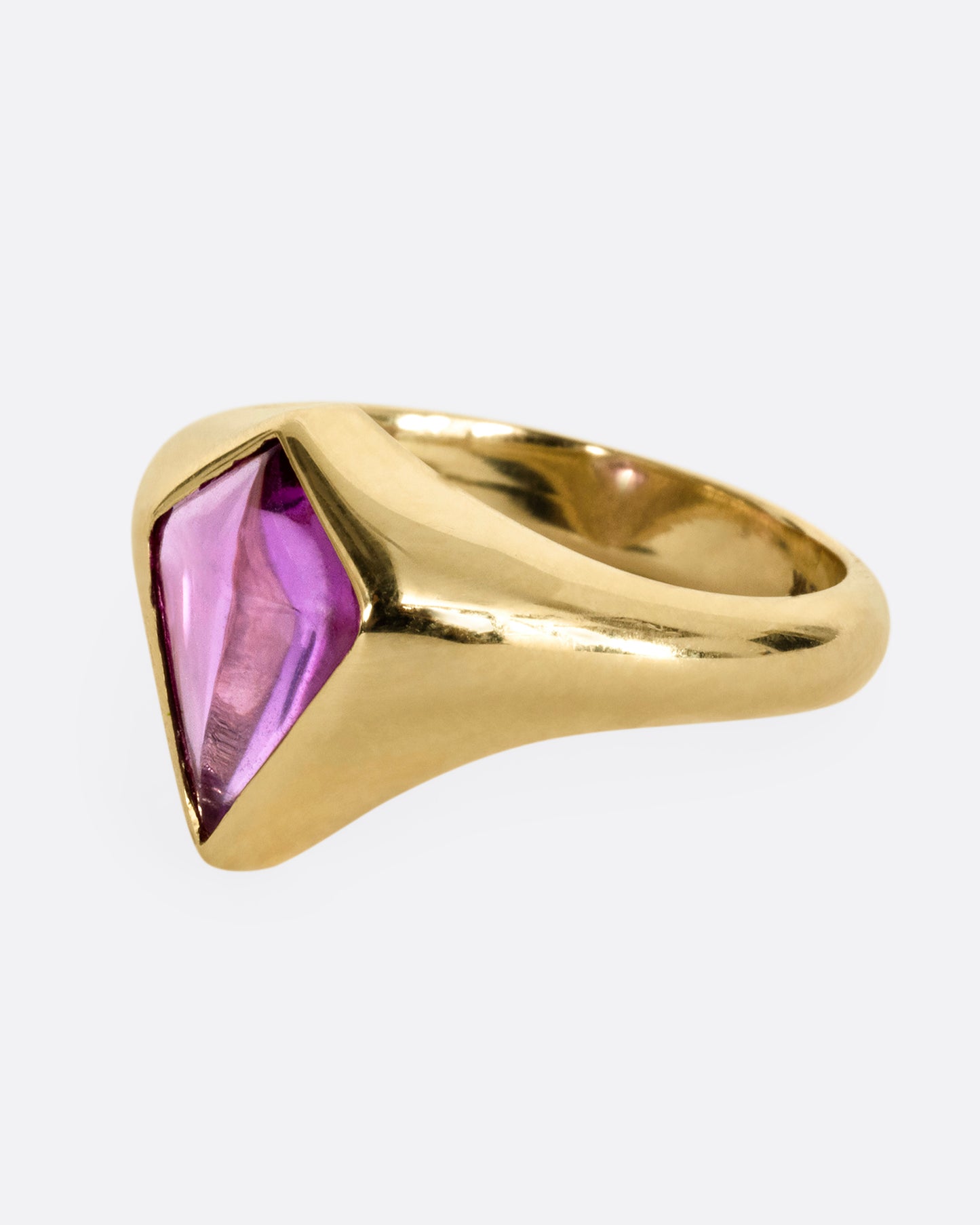 A yellow gold ring with a cabochon maroon kite shaped sapphire. Shown from the side.