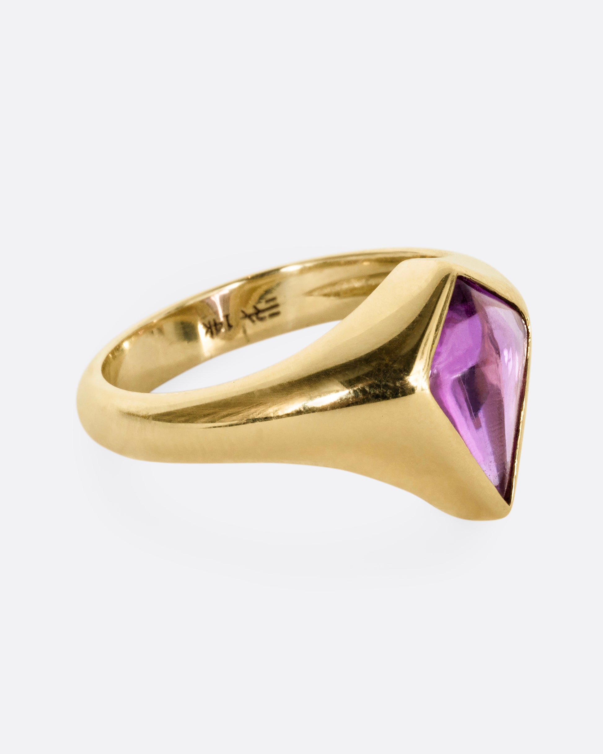 A yellow gold ring with a cabochon maroon kite shaped sapphire. Shown from the side.