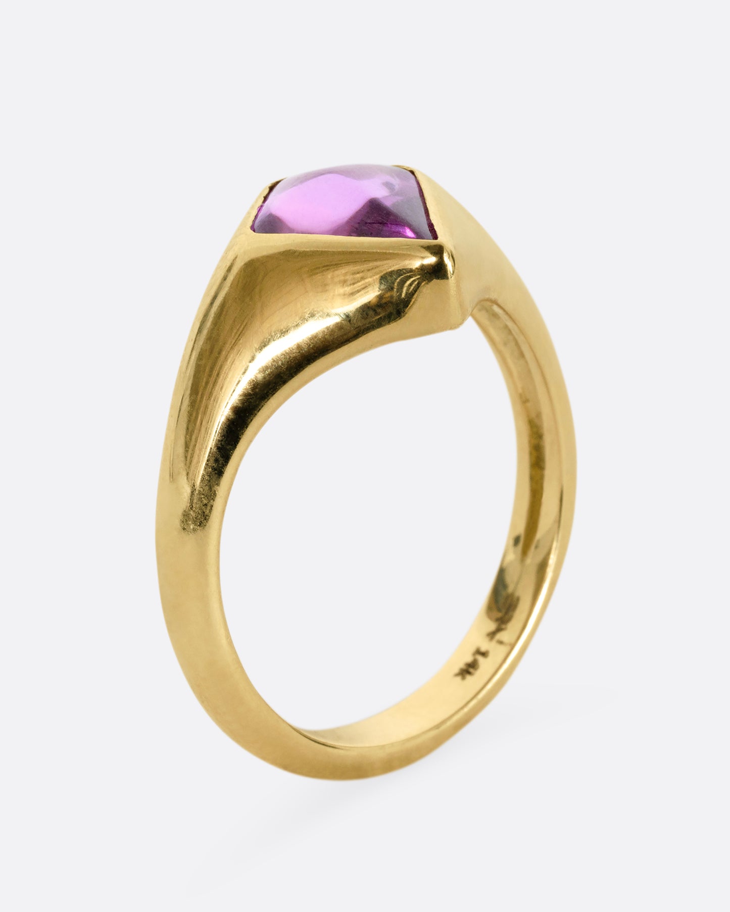 A yellow gold ring with a cabochon maroon kite shaped sapphire. Shown from the side, standing up.