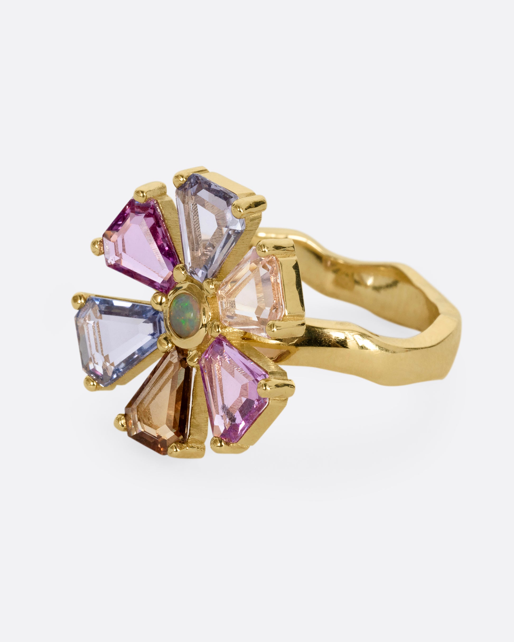 A yellow gold ring with a spinning flower made of multicolor sapphires. Shown from the side.