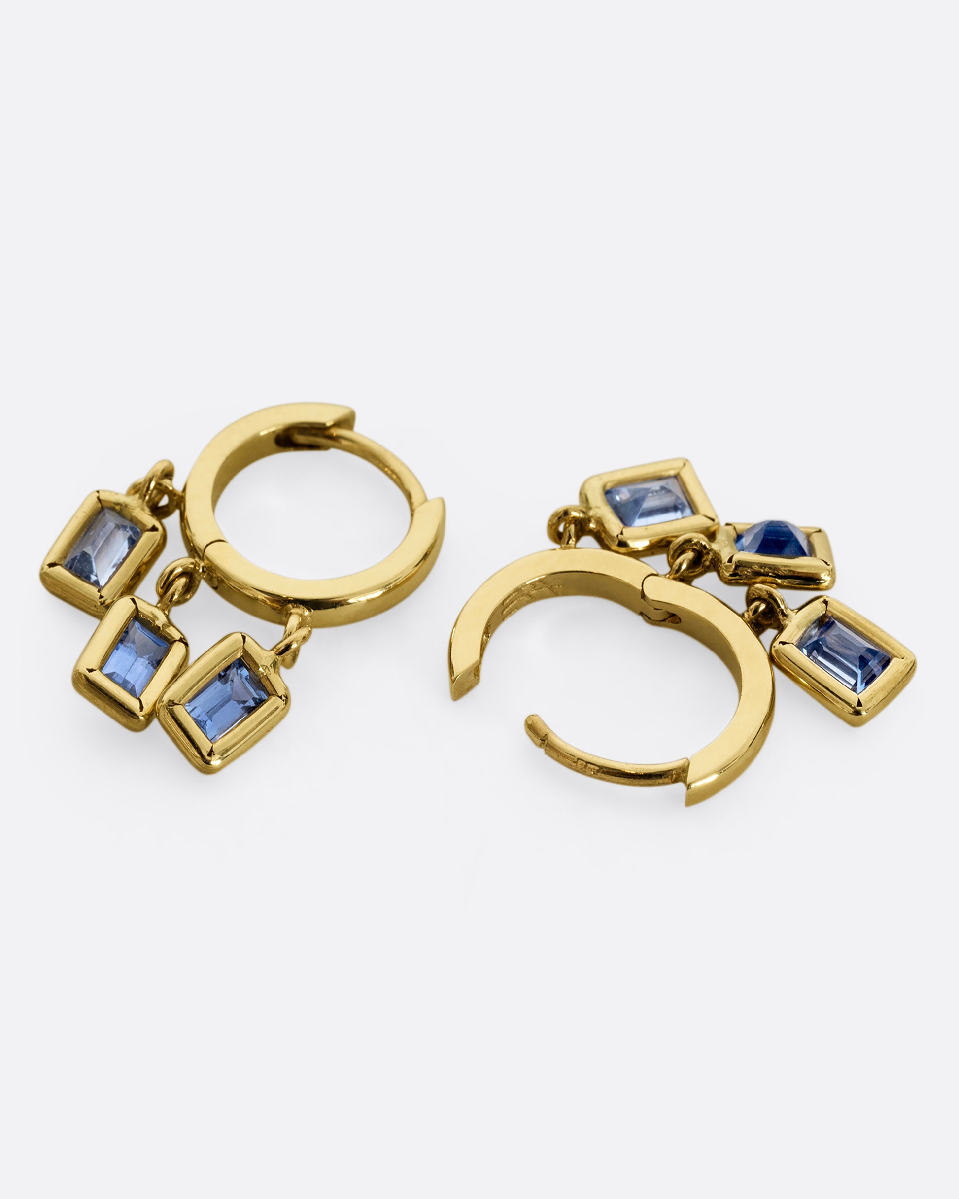 A yellow gold pair of hoop earrings with three dangling blue sapphires on each. Shown laying flat.