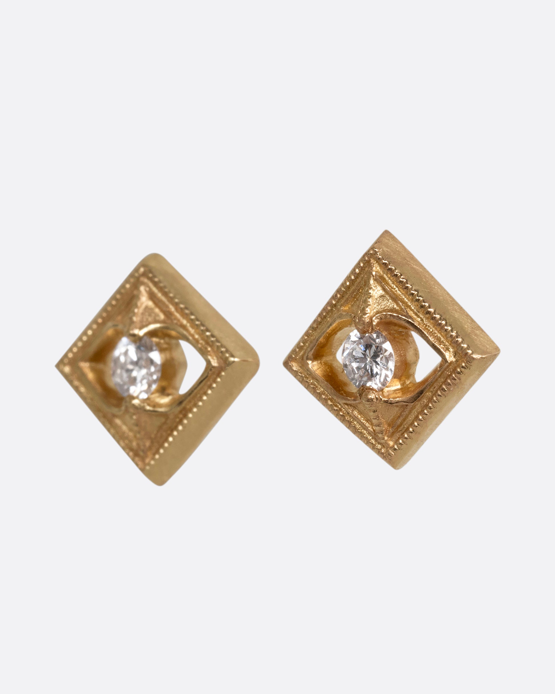 A pair of square yellow gold earrings with round diamonds at the center. Shown from the side.