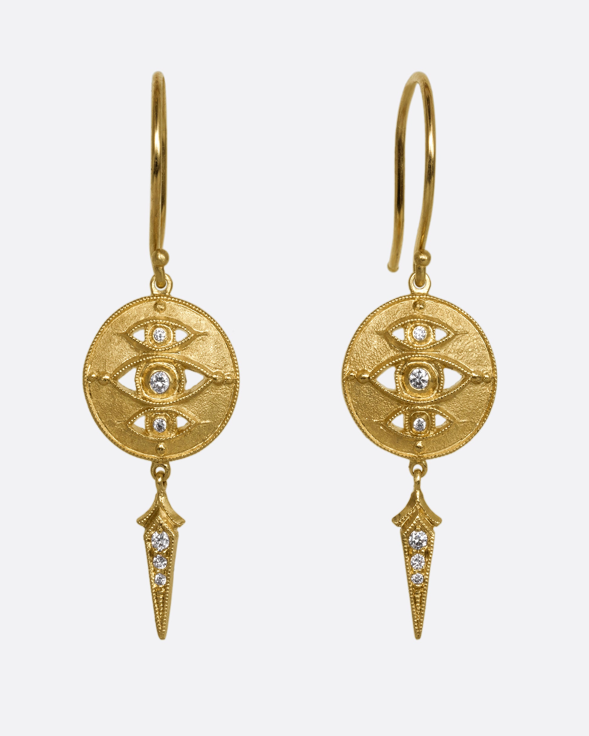 A pair of yellow gold drop earrings with diamond eyes on a disk and a spear shaped dangle. Shown from the front.