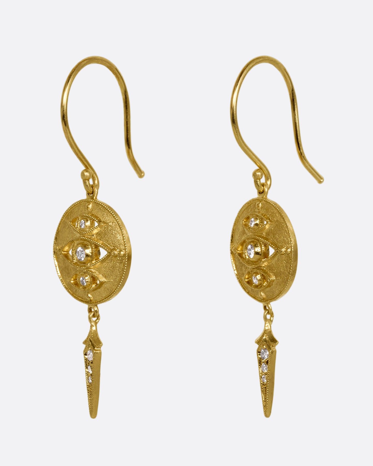 A pair of yellow gold drop earrings with diamond eyes on a disk and a spear shaped dangle. Shown from the side.