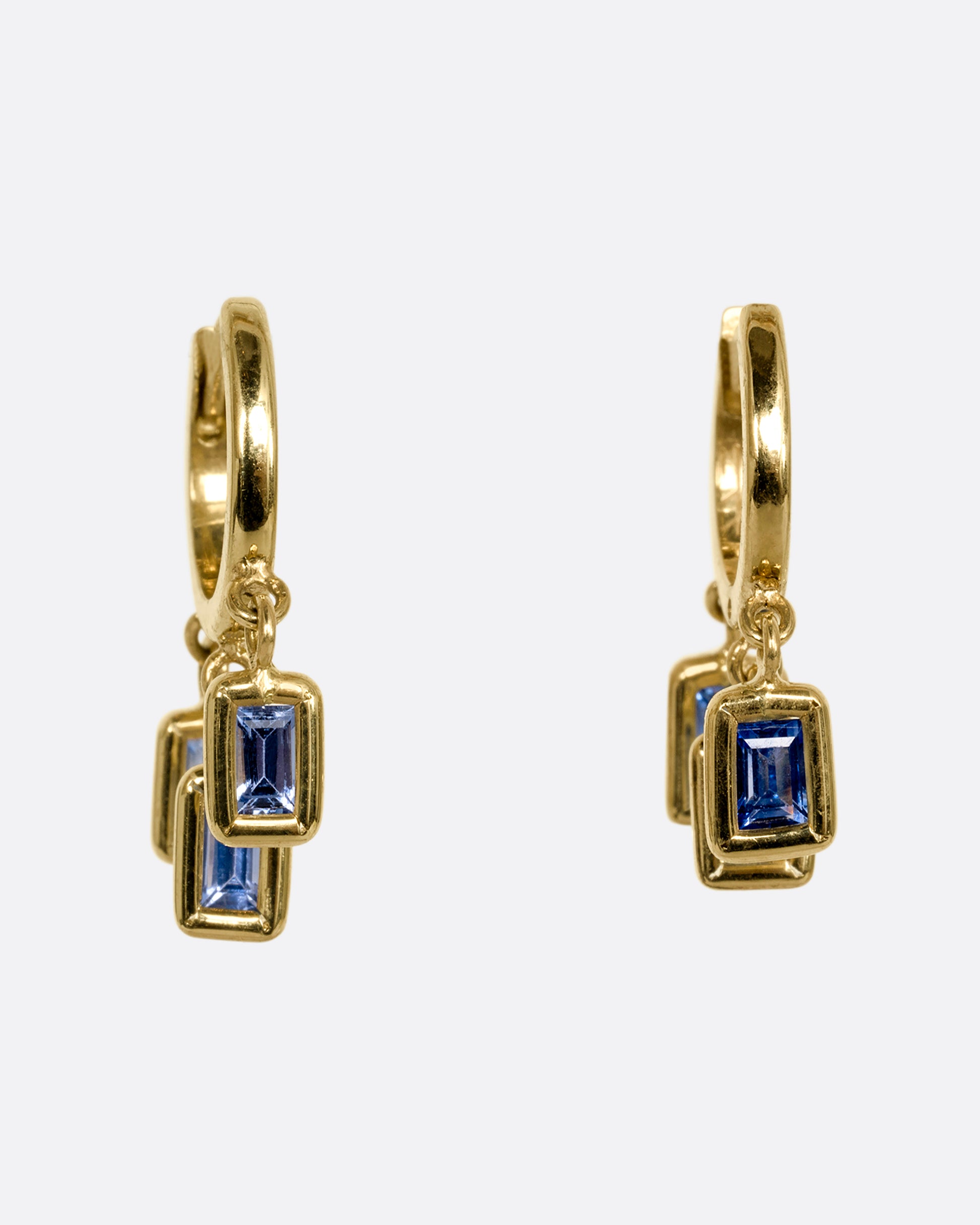 A yellow gold pair of hoop earrings with three dangling blue sapphires on each. Shown form the front.