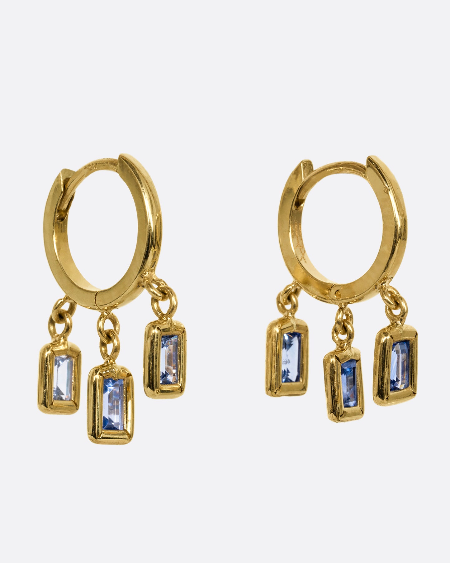 A yellow gold pair of hoop earrings with three dangling blue sapphires on each. Shown from the side.