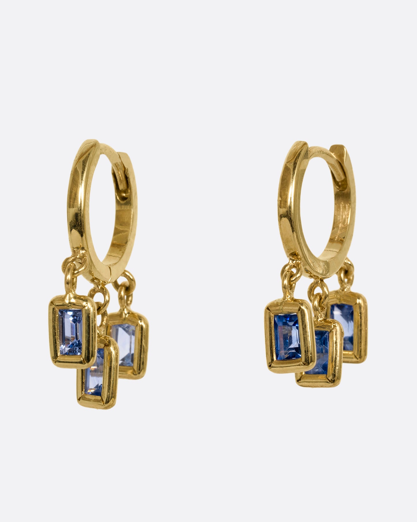 A yellow gold pair of hoop earrings with three dangling blue sapphires on each. Shown slightly from the side.