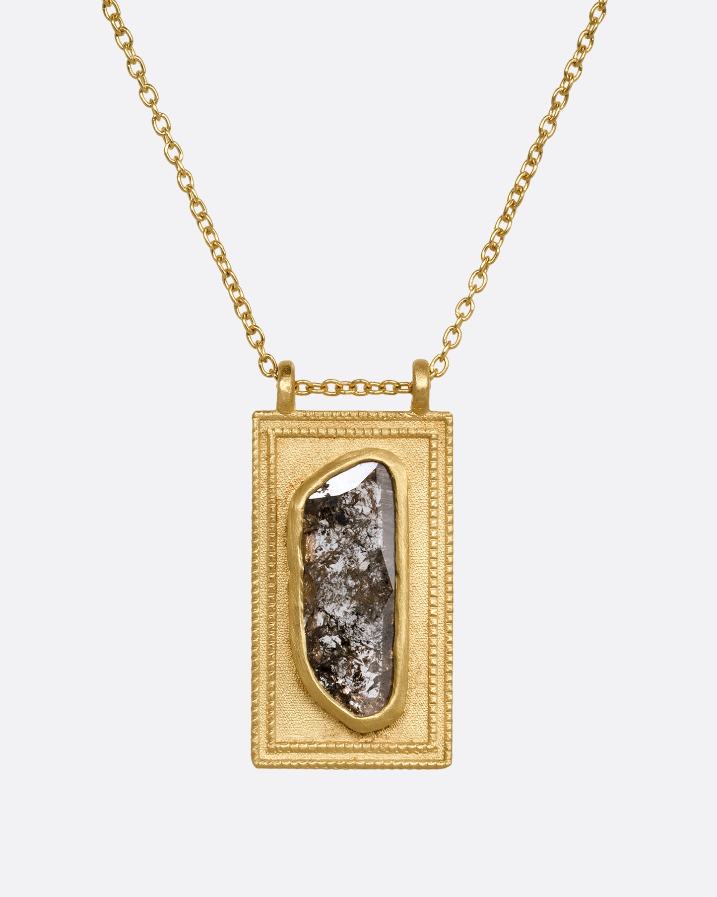 A yellow gold necklace with a rectangular pendant holding a salt and pepper diamond. Shown close up from the front.